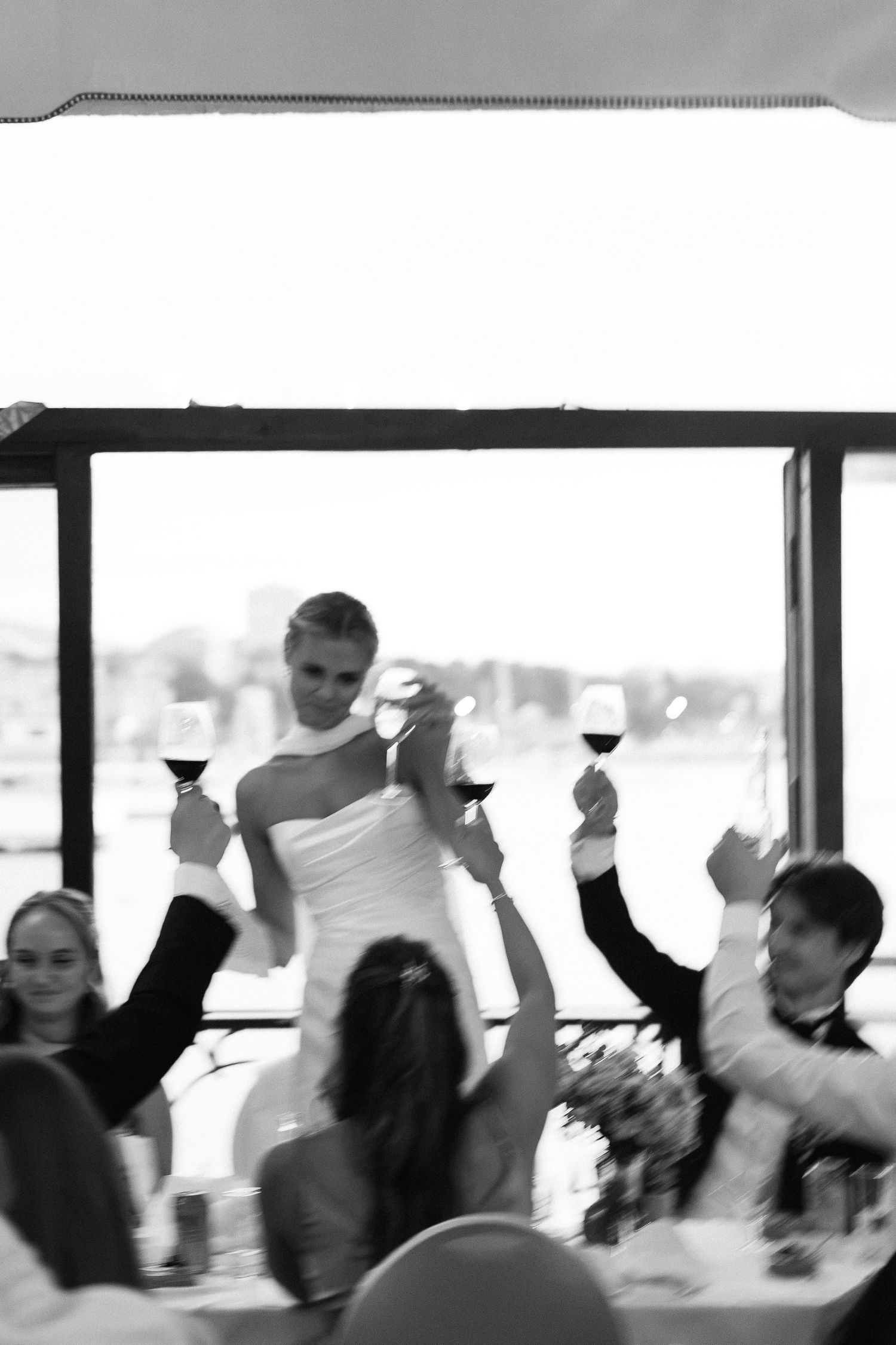 Black and white photo of bride and wedding guests raising wine glasses in a toast at reception.