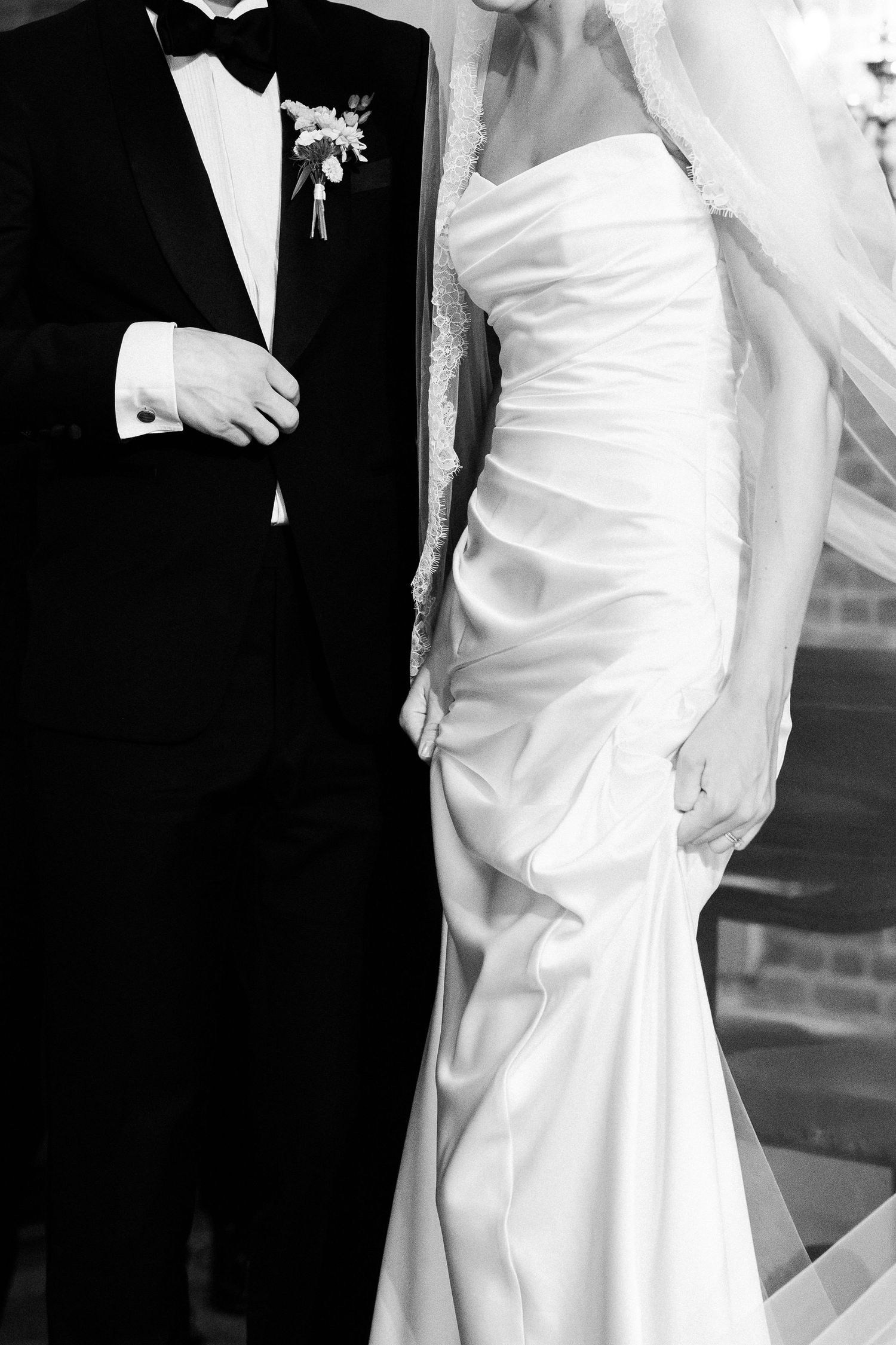 Black and white photo of a bride in elegant white gown and groom in tuxedo standing together at their wedding ceremony.