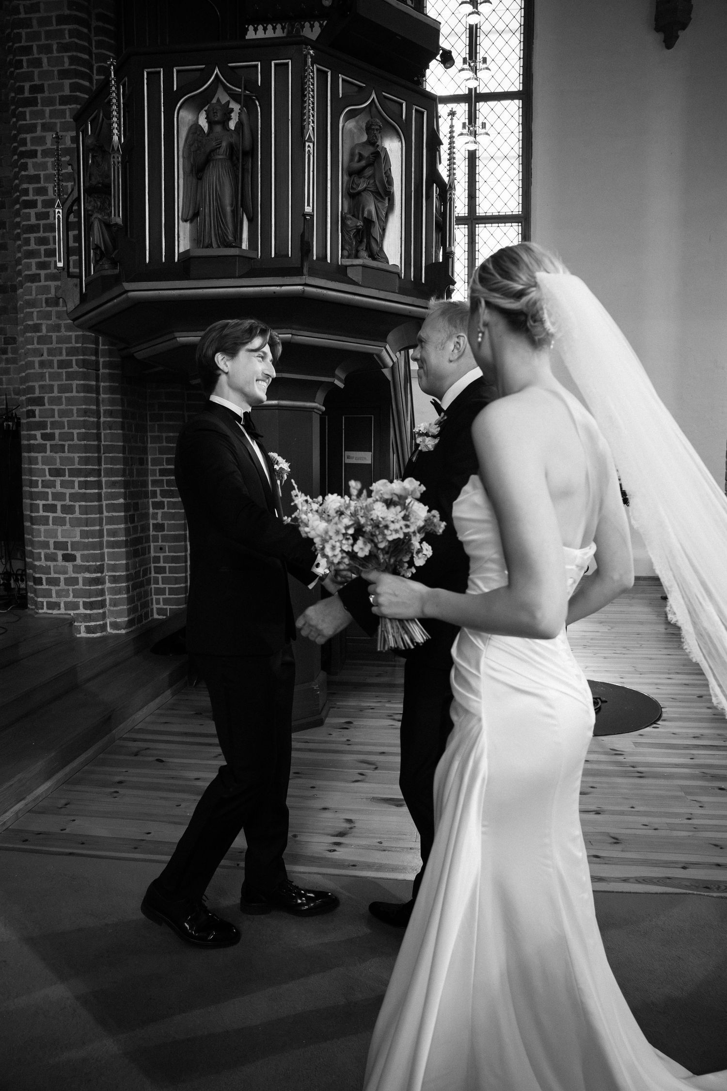 Bride and groom share a tender moment with officiant during an elegant black and white church wedding ceremony.