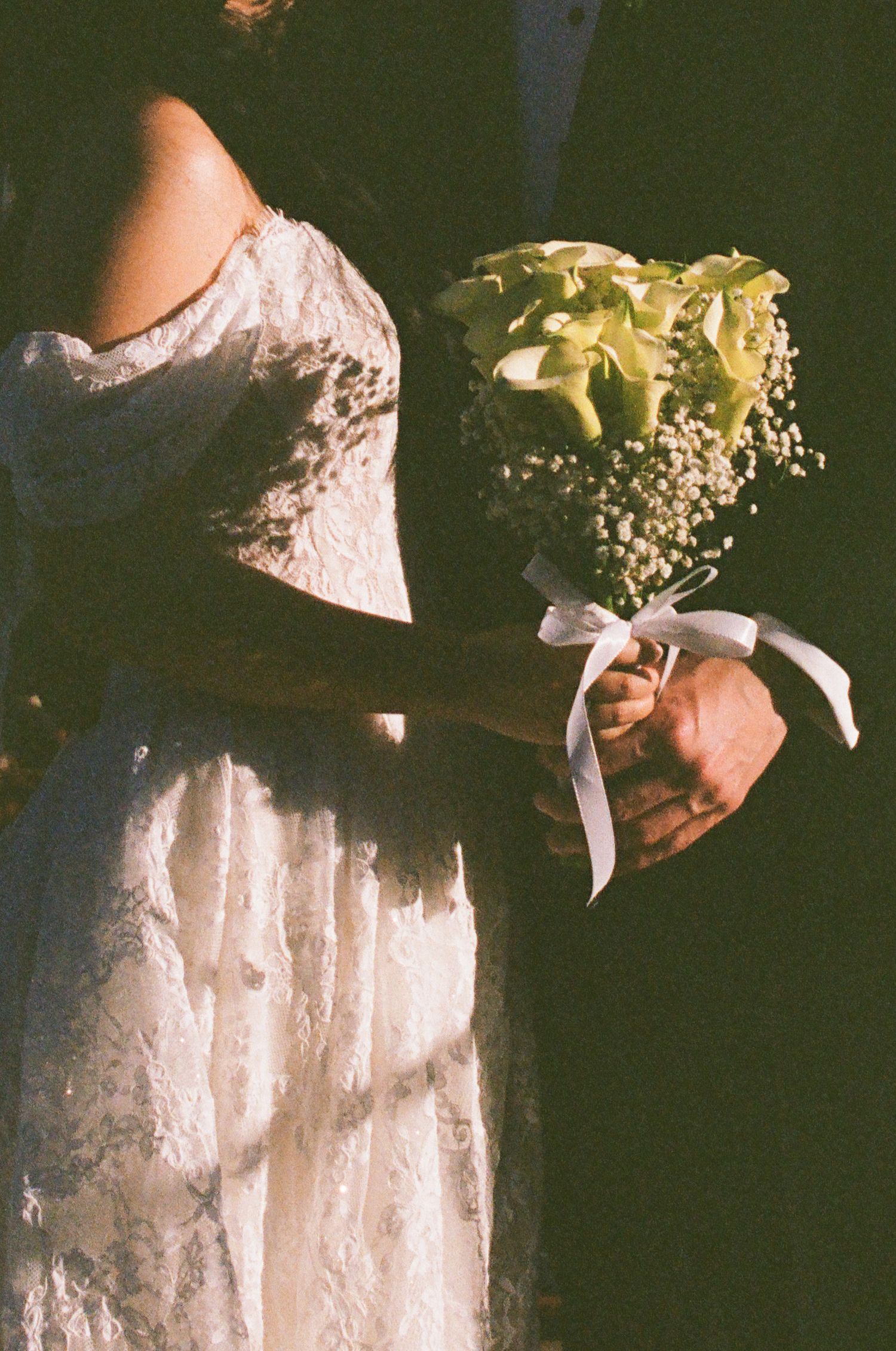 Bride in lace wedding dress holds bouquet of green calla lilies and baby's breath with white ribbon.