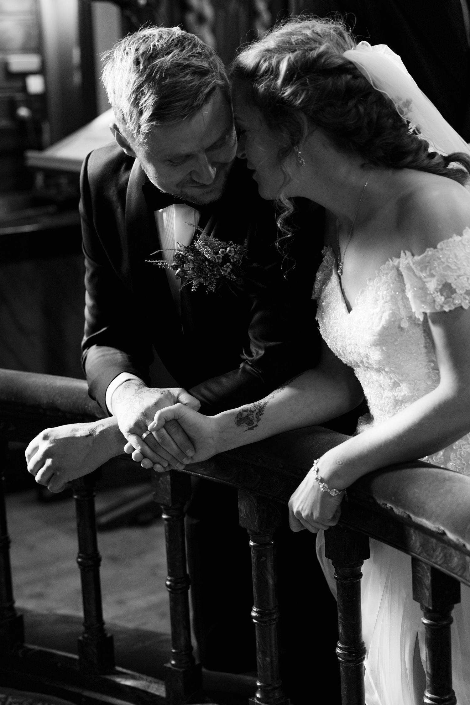 Black and white photo of a bride and groom leaning on a wooden railing, holding hands and sharing a tender, smiling moment. Ler Trøndelag