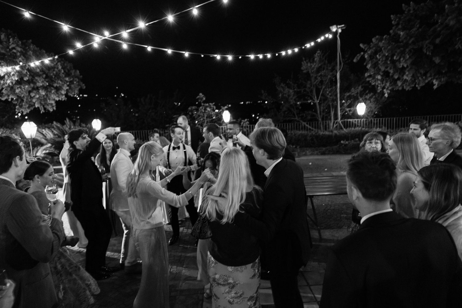 Guests dance under string lights at elegant outdoor wedding reception at night.