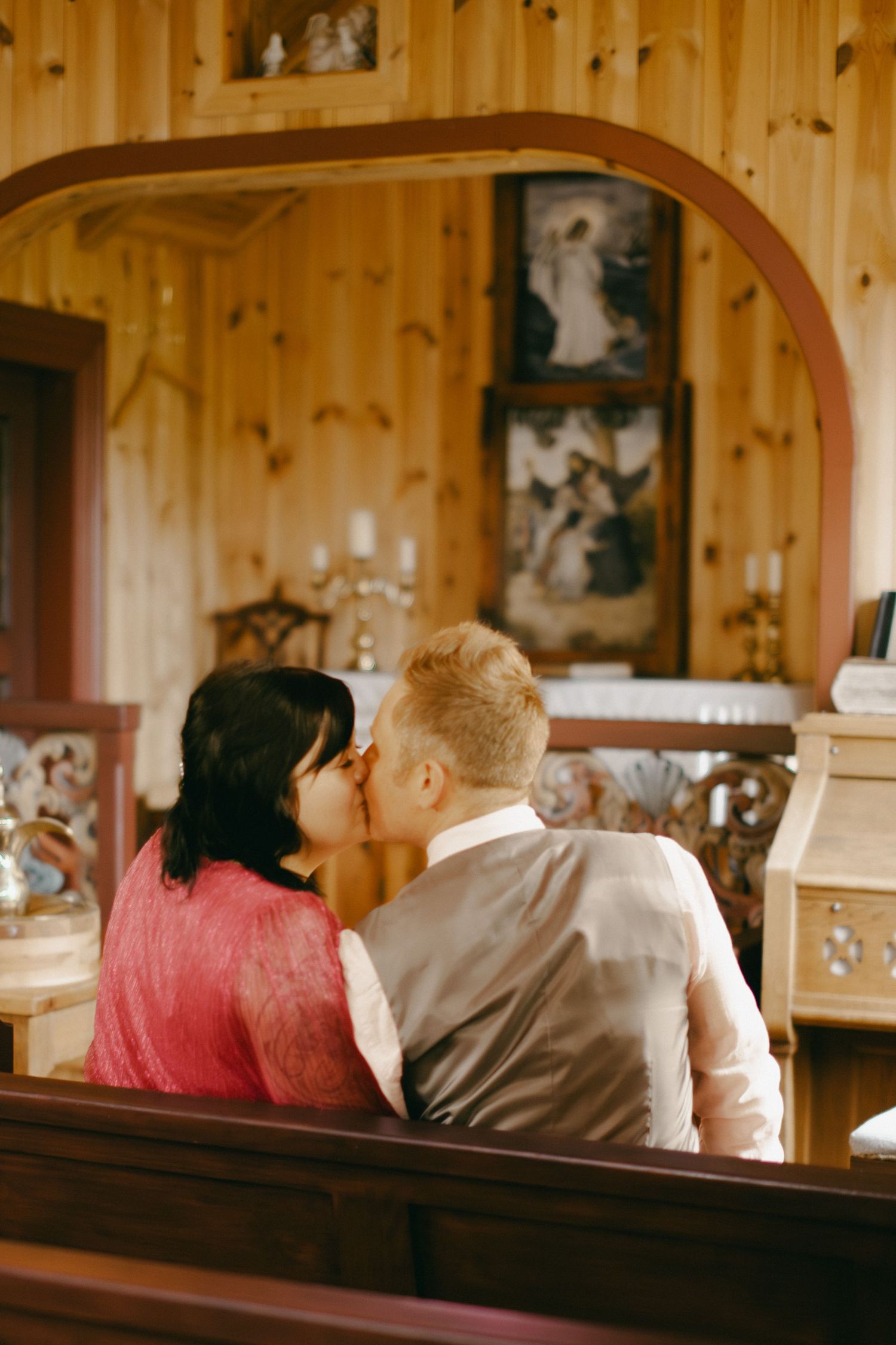 Couple sharing a kiss in a wooden church pew during their intimate wedding ceremony.