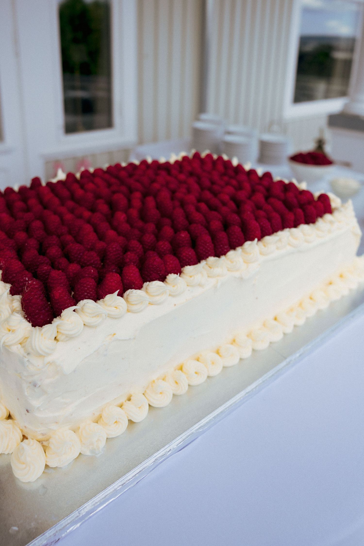 Elegant rectangular white wedding cake topped with fresh red raspberries and cream rosettes.