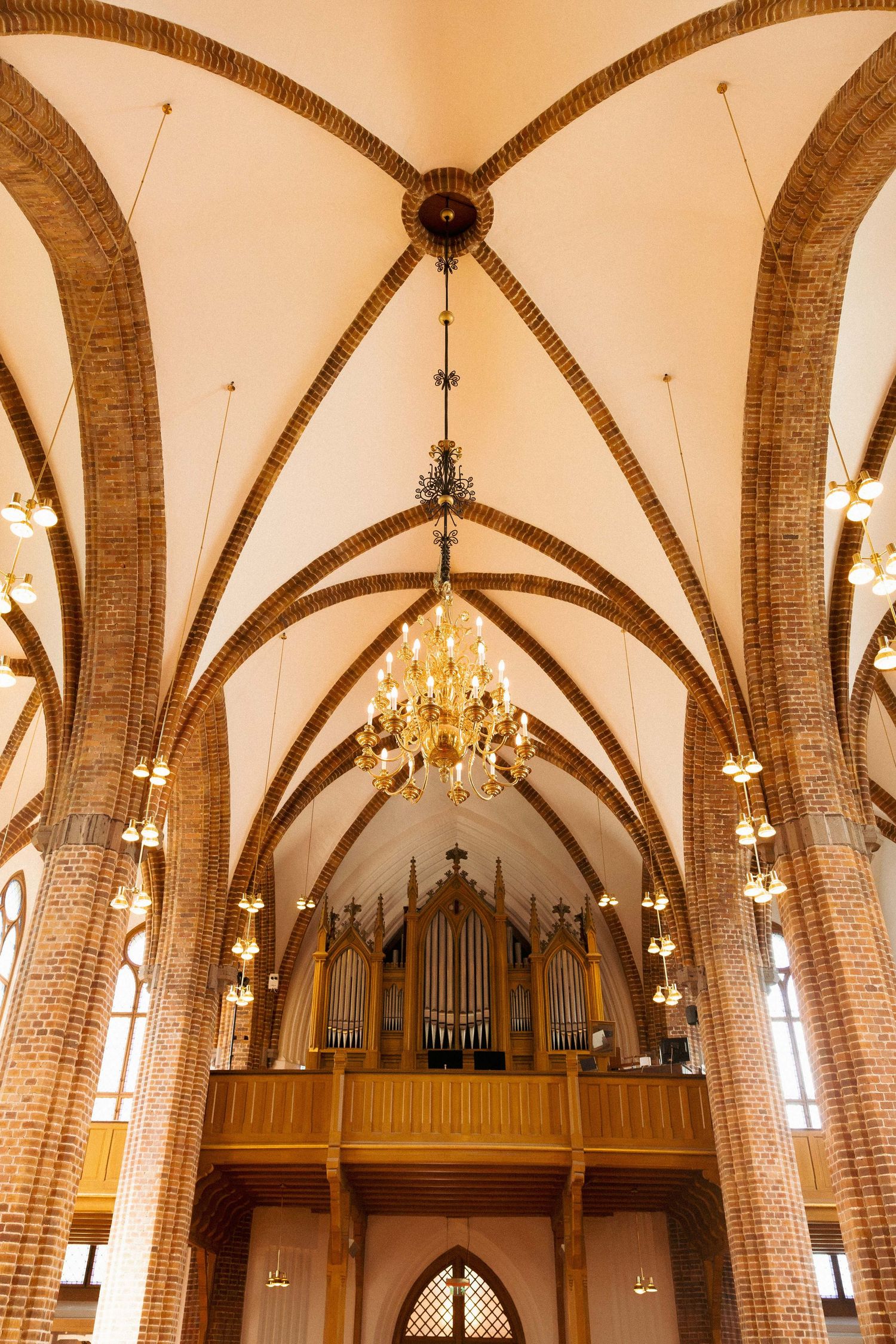 Gothic church interior with brick arched ceiling, ornate chandelier, and pipe organ on wooden balcony.