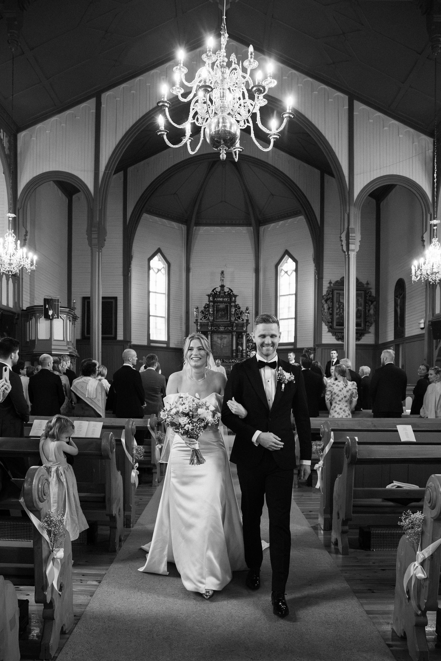 Black and white photo of smiling bride and groom walking down church aisle after wedding ceremony.