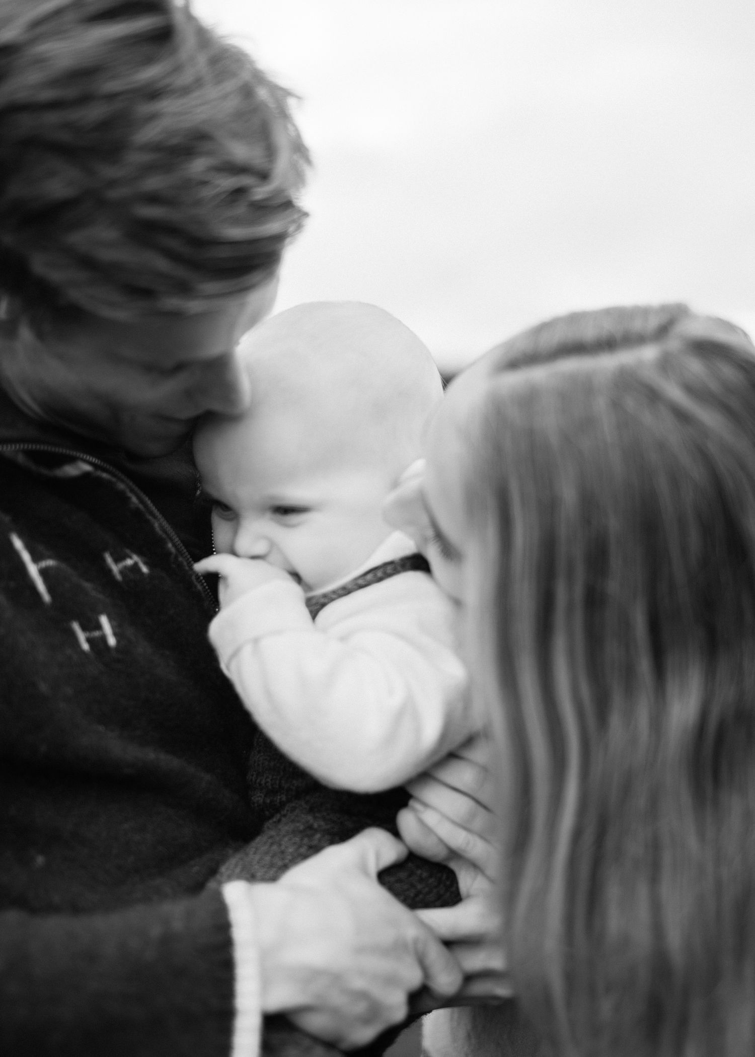Black and white photo of two parents lovingly holding and kissing their newborn baby.