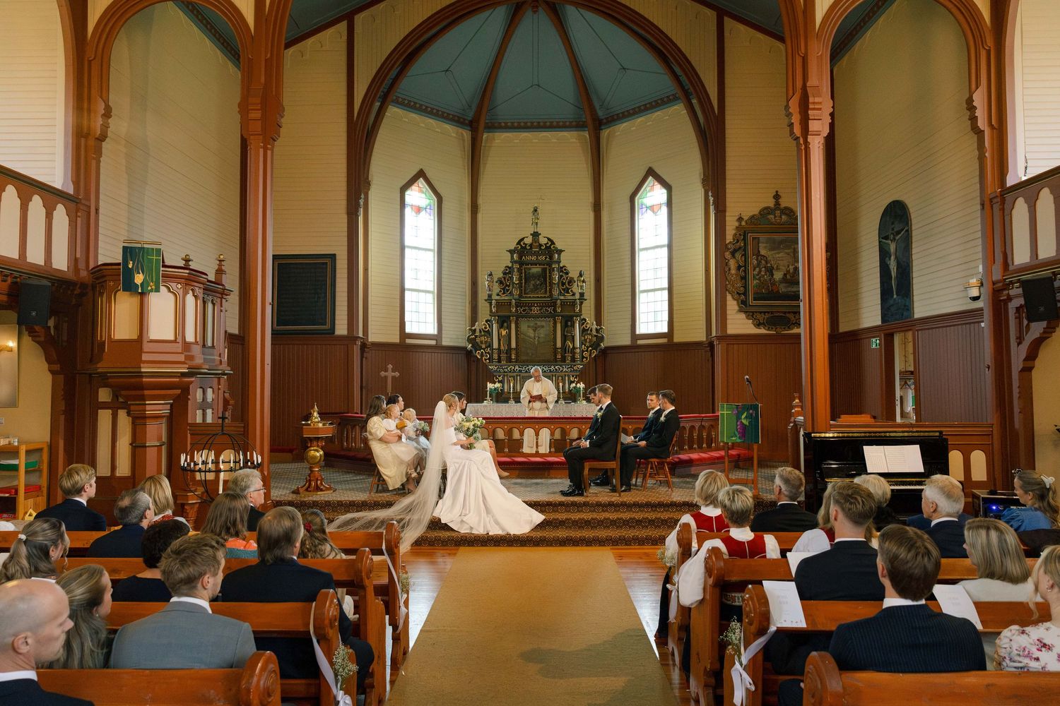 Wedding ceremony inside a traditional wooden church with guests seated in pews.