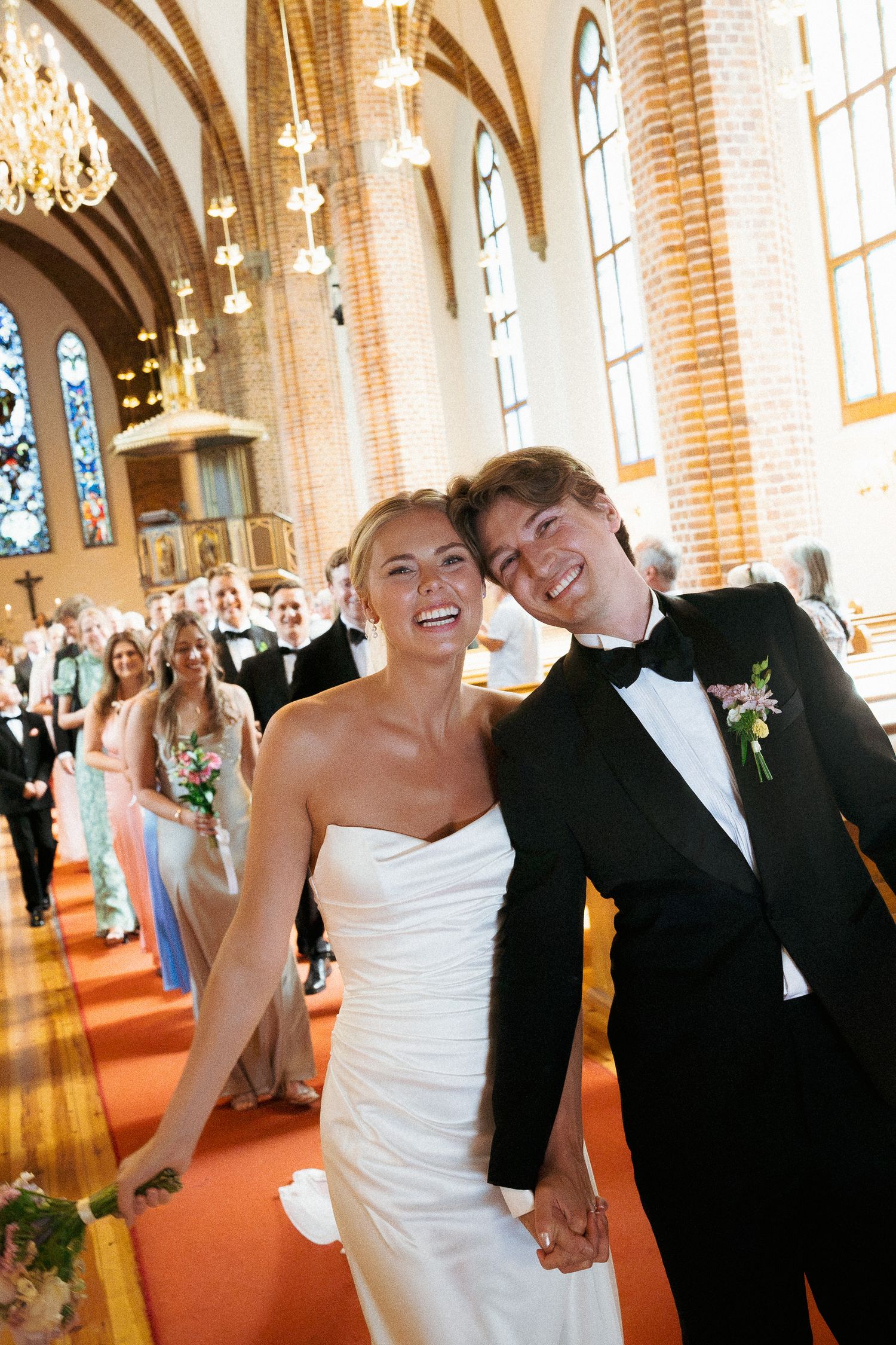 Joyful bride and groom walking down church aisle after wedding ceremony, holding hands and smiling.