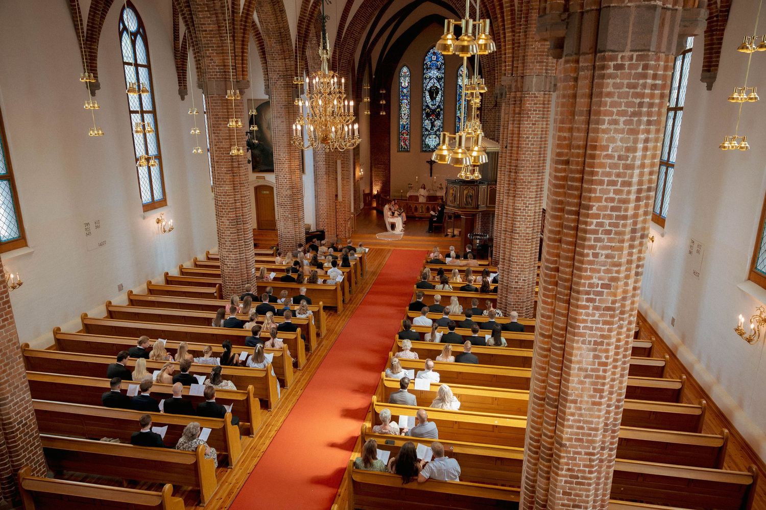 Aerial view of a historic brick church interior with red carpet aisle, wooden pews, and ornate chandeliers during a service.
