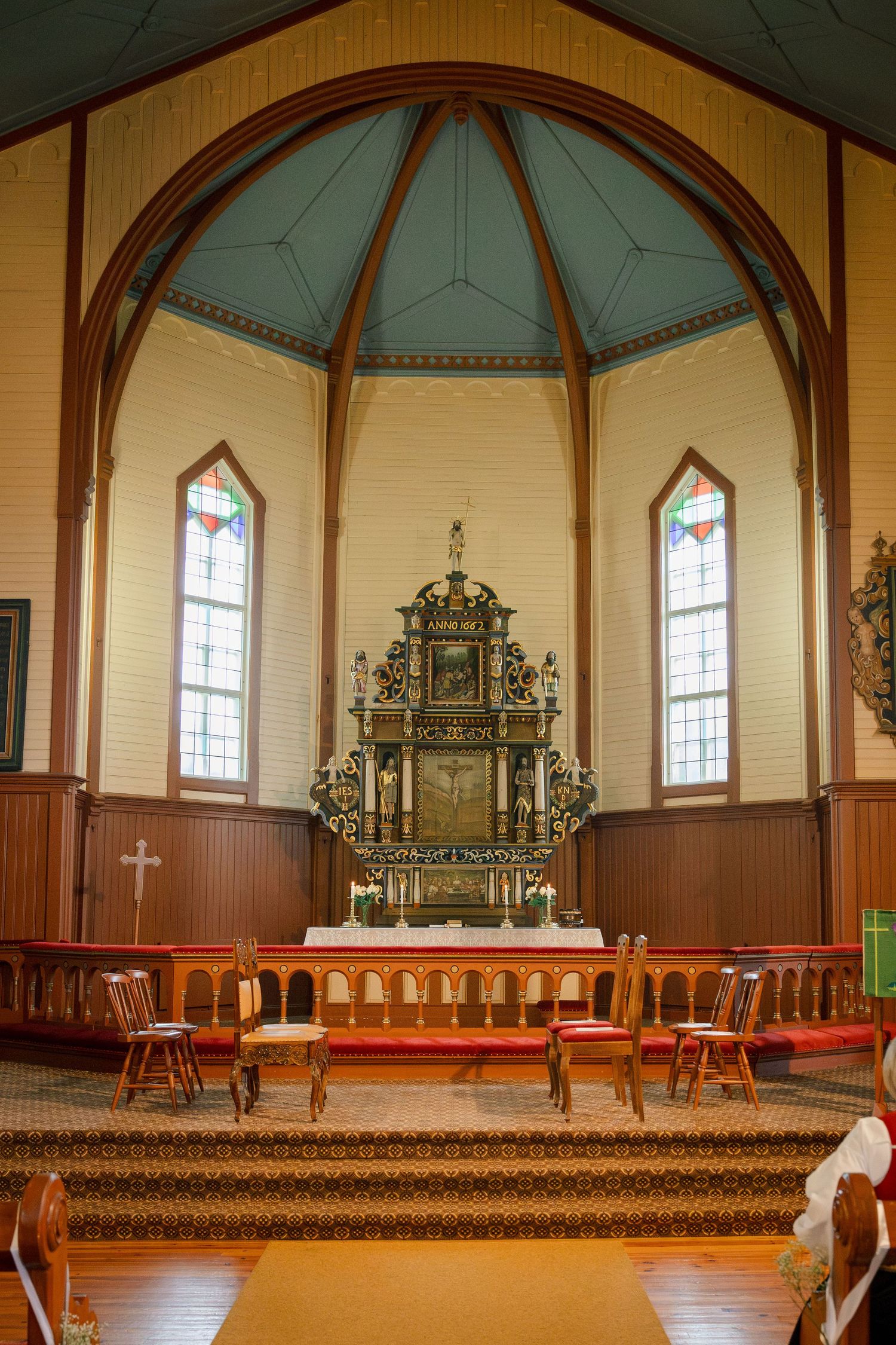 Interior of a historic wooden church featuring ornate altar, stained glass windows, and arched ceiling.