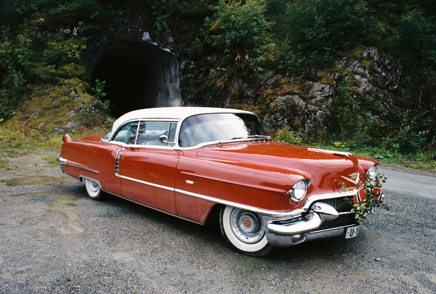 Vintage red 1956 Cadillac wedding car decorated with flowers parked near tunnel.