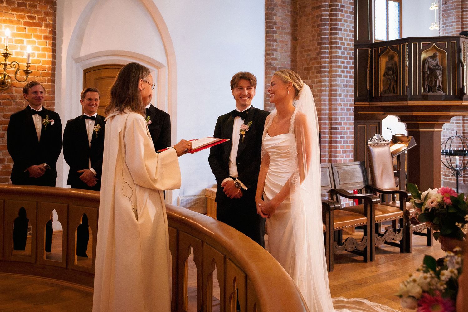 A bride and groom exchange vows with an officiant in a beautiful brick church during their wedding ceremony.