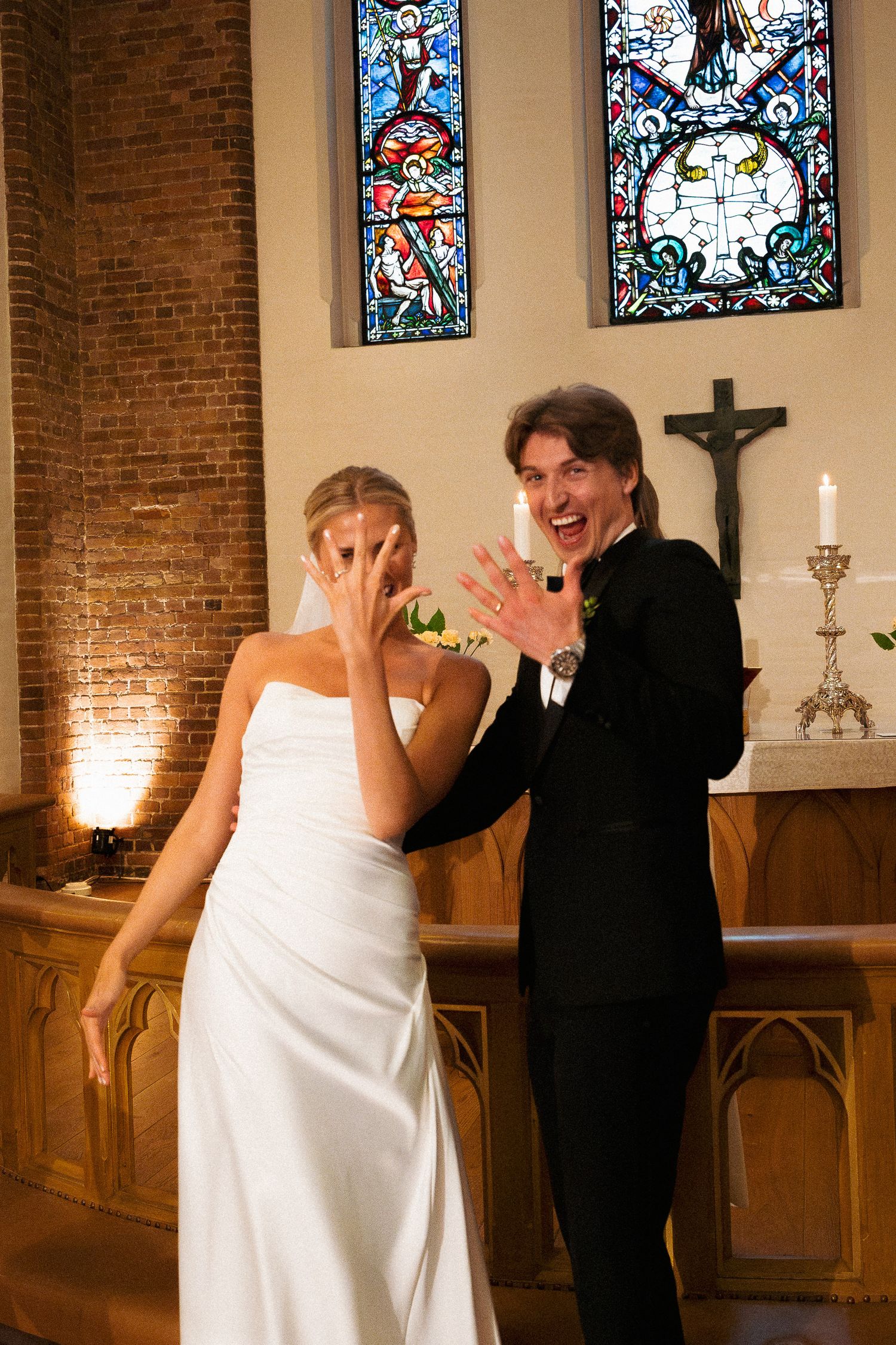 Bride in white gown and groom in black suit celebrating at church altar.