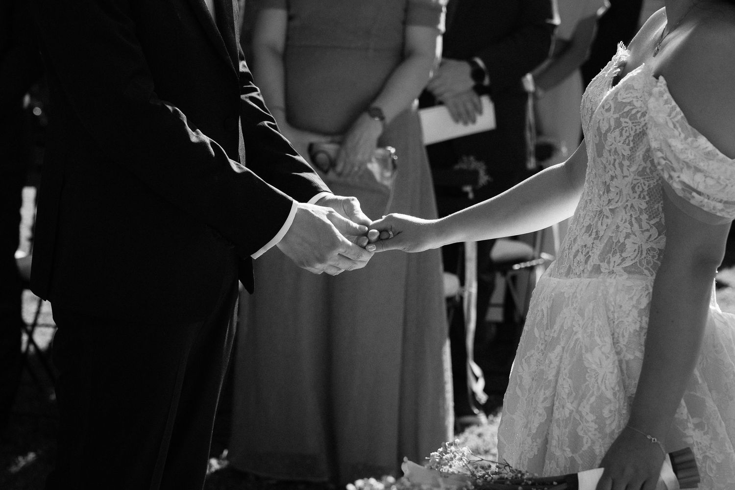 Black and white photo of bride and groom holding hands during wedding ceremony.