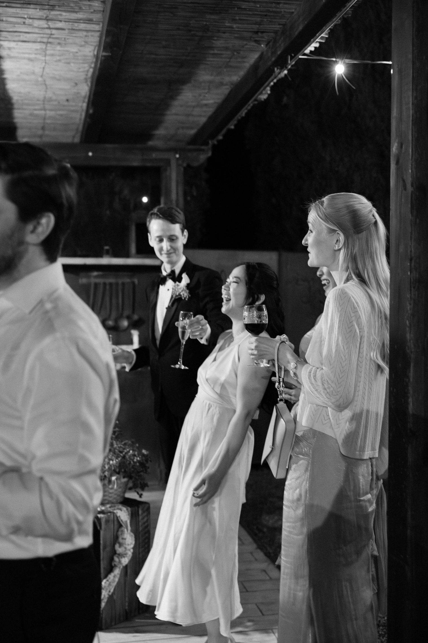 Black and white photo of wedding guests socializing with wine glasses at an evening reception.