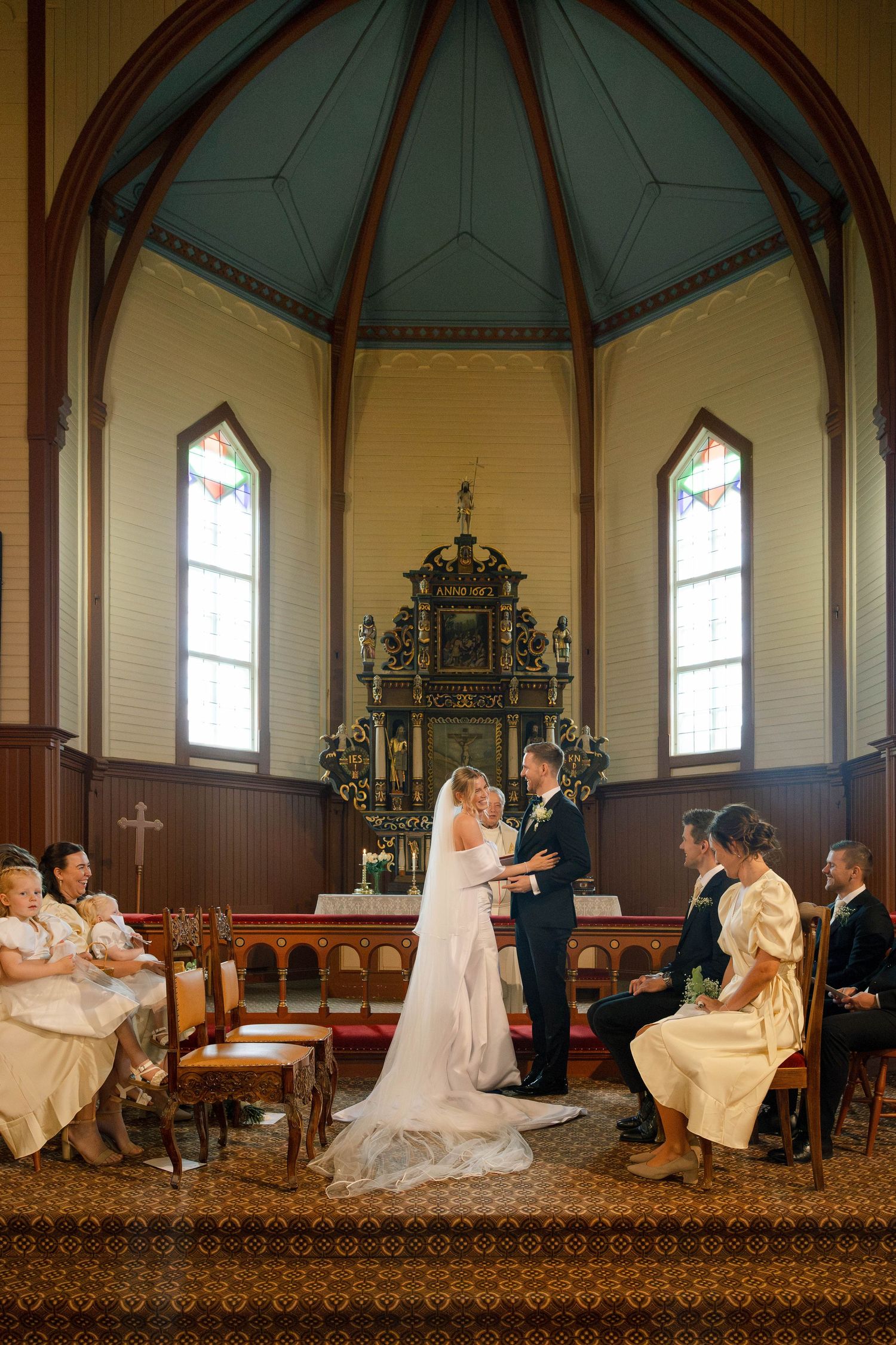 Bride and groom exchange vows at altar in charming octagonal church chapel with wooden decor and stained glass.