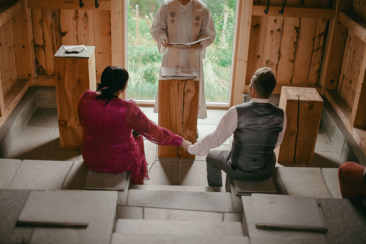 Couple holds hands during intimate wedding ceremony officiated indoors at a rustic wooden chapel.