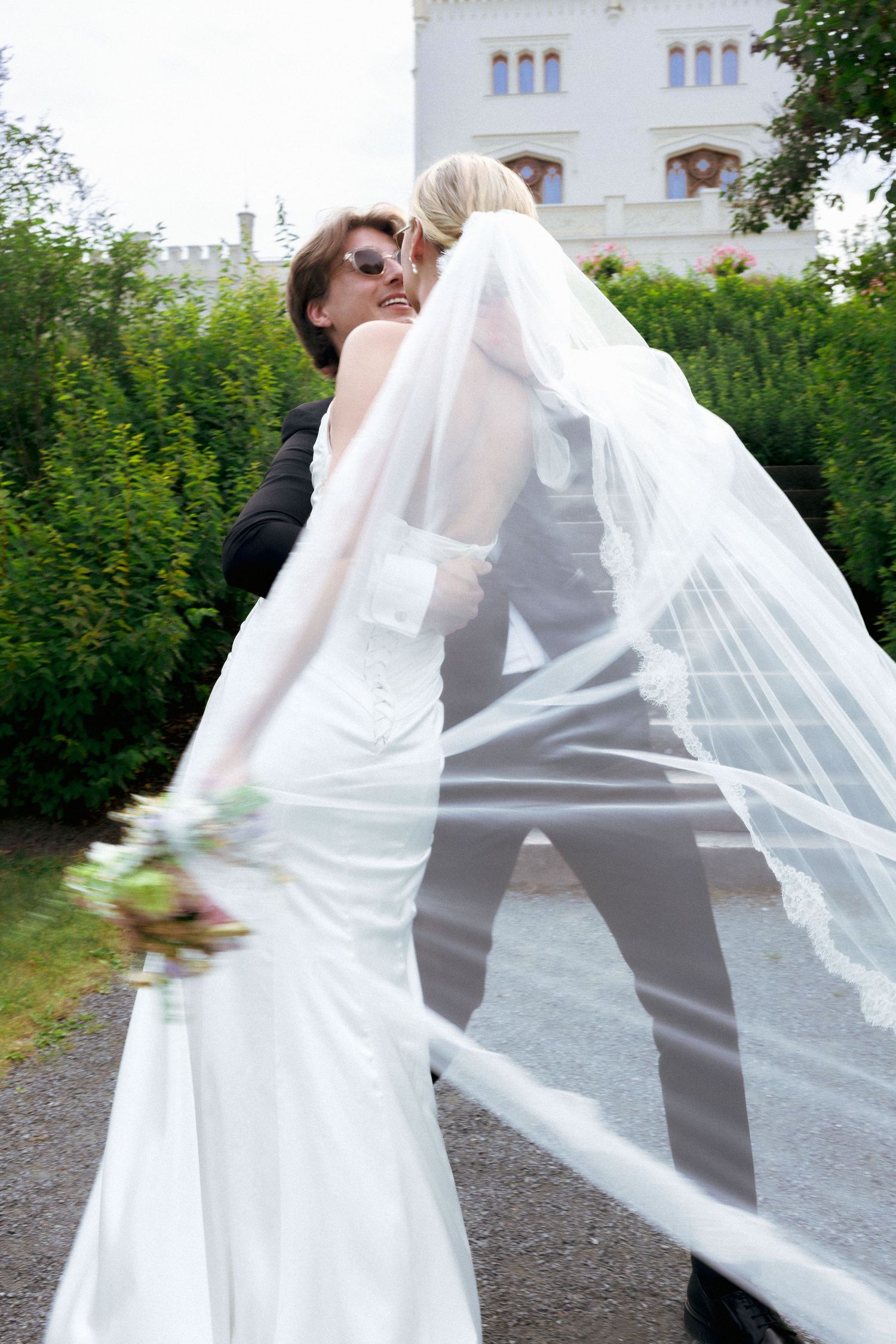 Newlywed couple shares romantic kiss outdoors with bride's veil flowing dramatically in the wind.