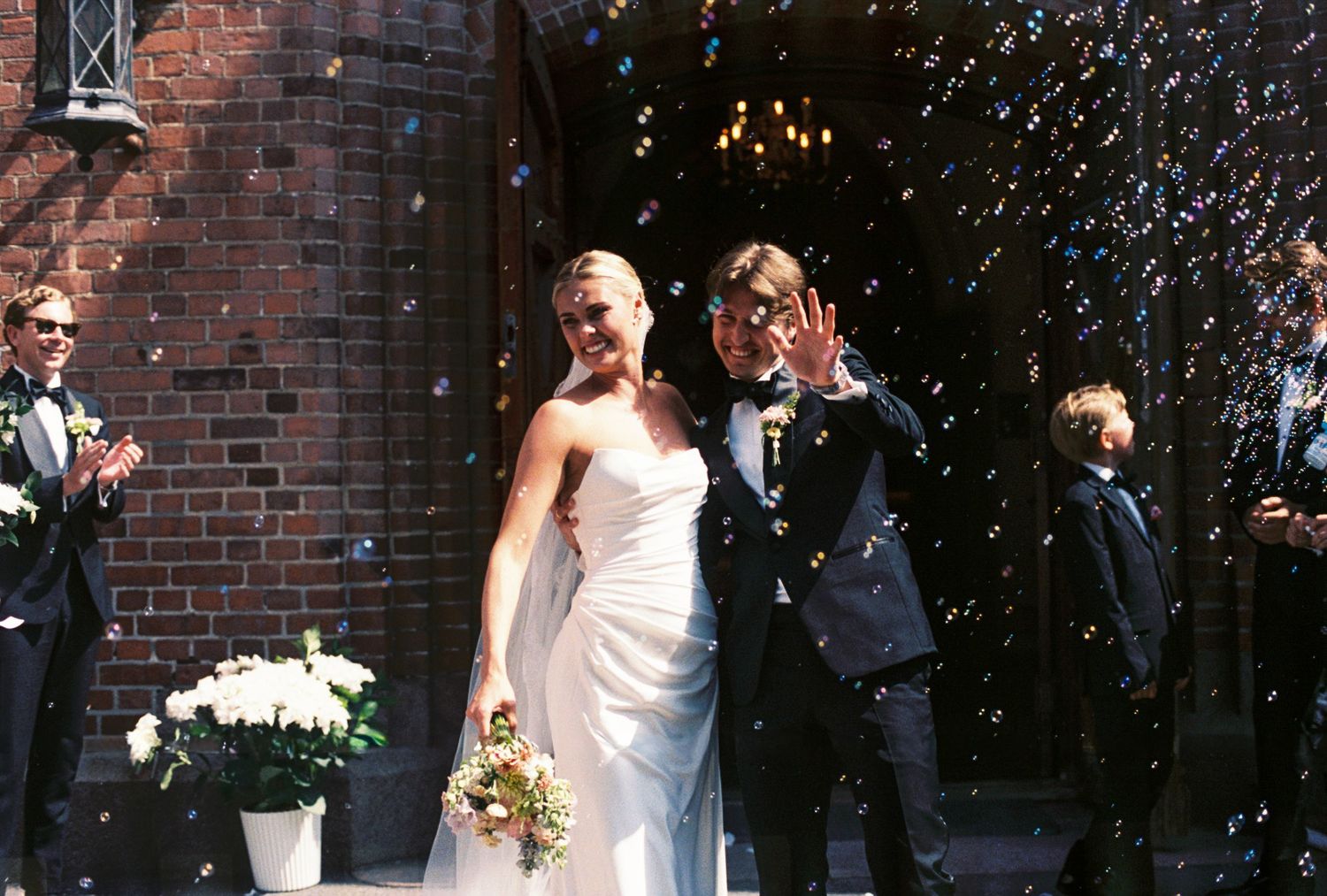 Newlyweds exit church amid confetti shower as guests celebrate outside.