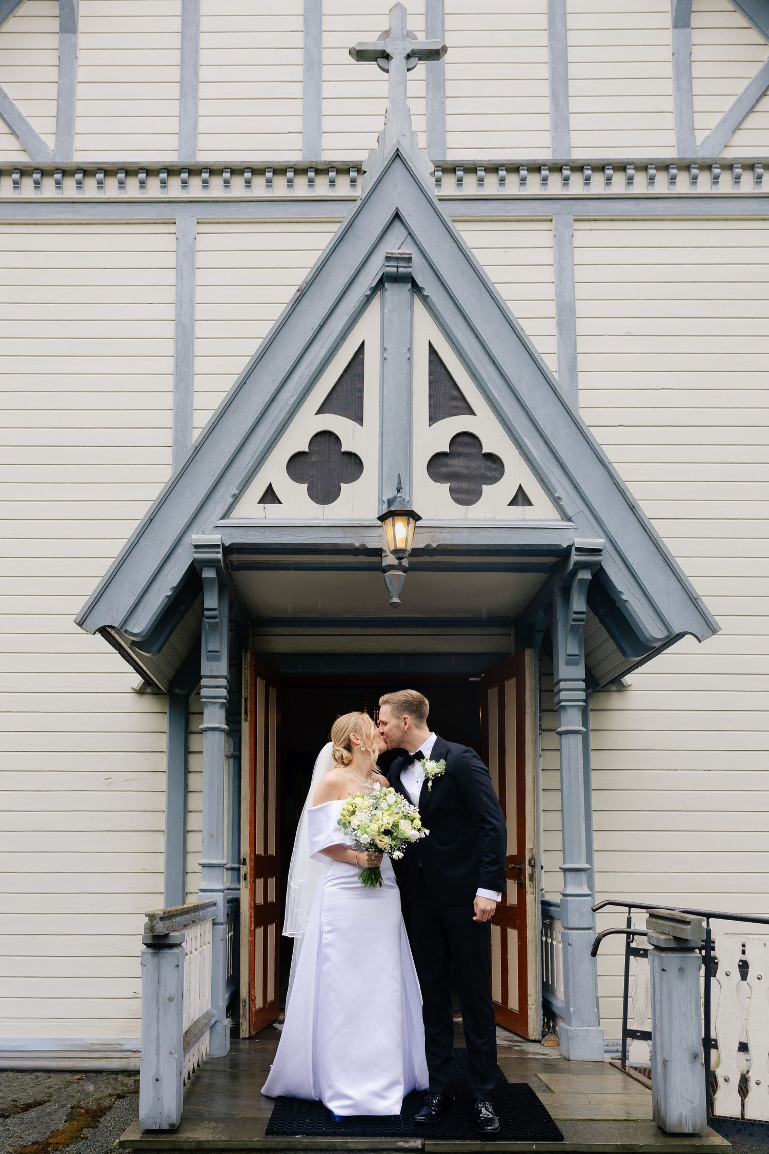 Bride and groom kissing at entrance of white wooden church after wedding ceremony.
