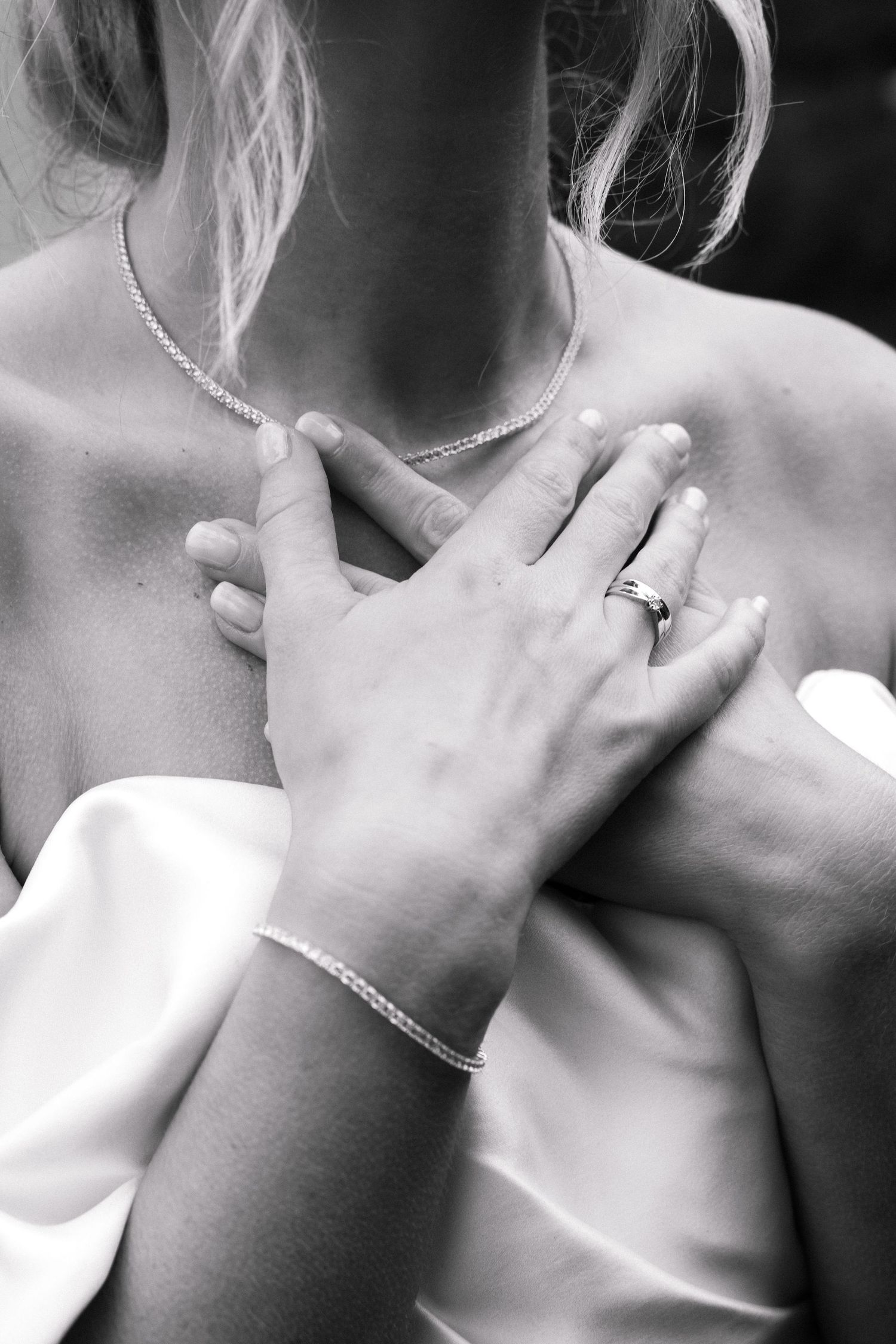 Black and white photo of a bride with hands on chest, wearing a diamond ring, bracelet, and pearl necklace.
