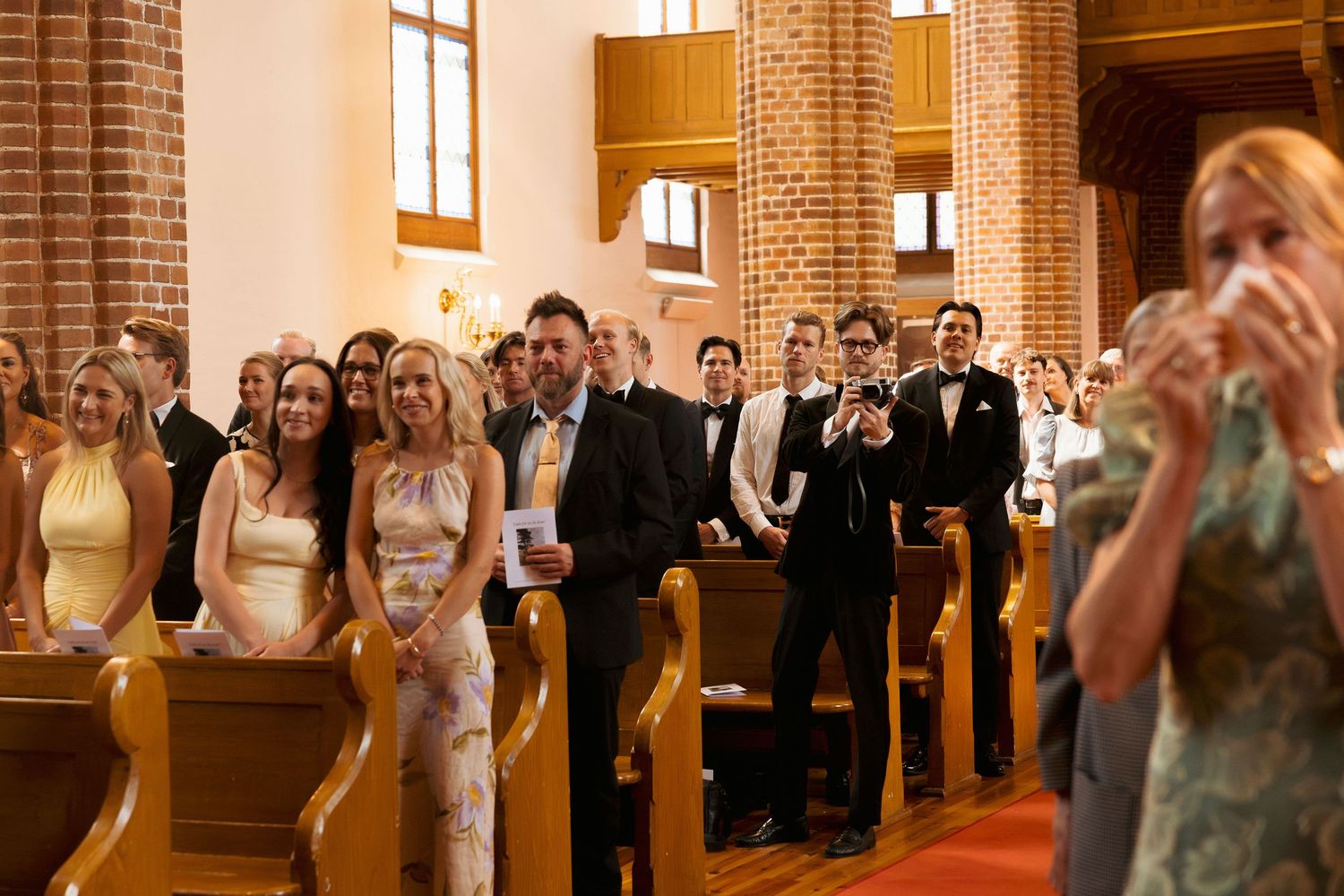 Wedding guests seated in church pews smiling and applauding during ceremony.