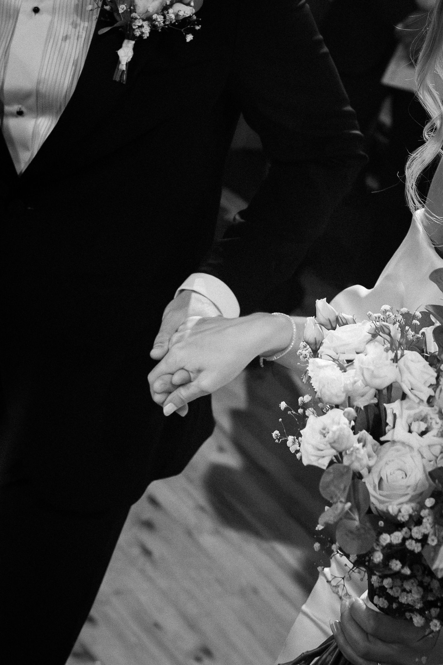 Black and white photo of bride and groom holding hands with bridal bouquet of white roses.