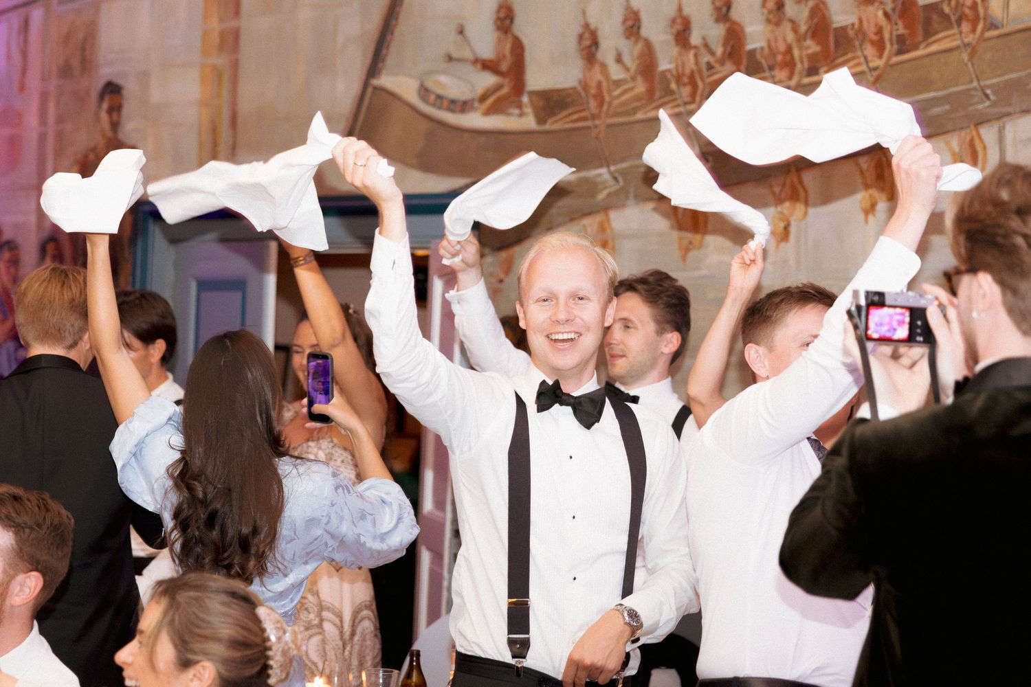 Guests waving white napkins on dance floor during lively wedding reception celebration.