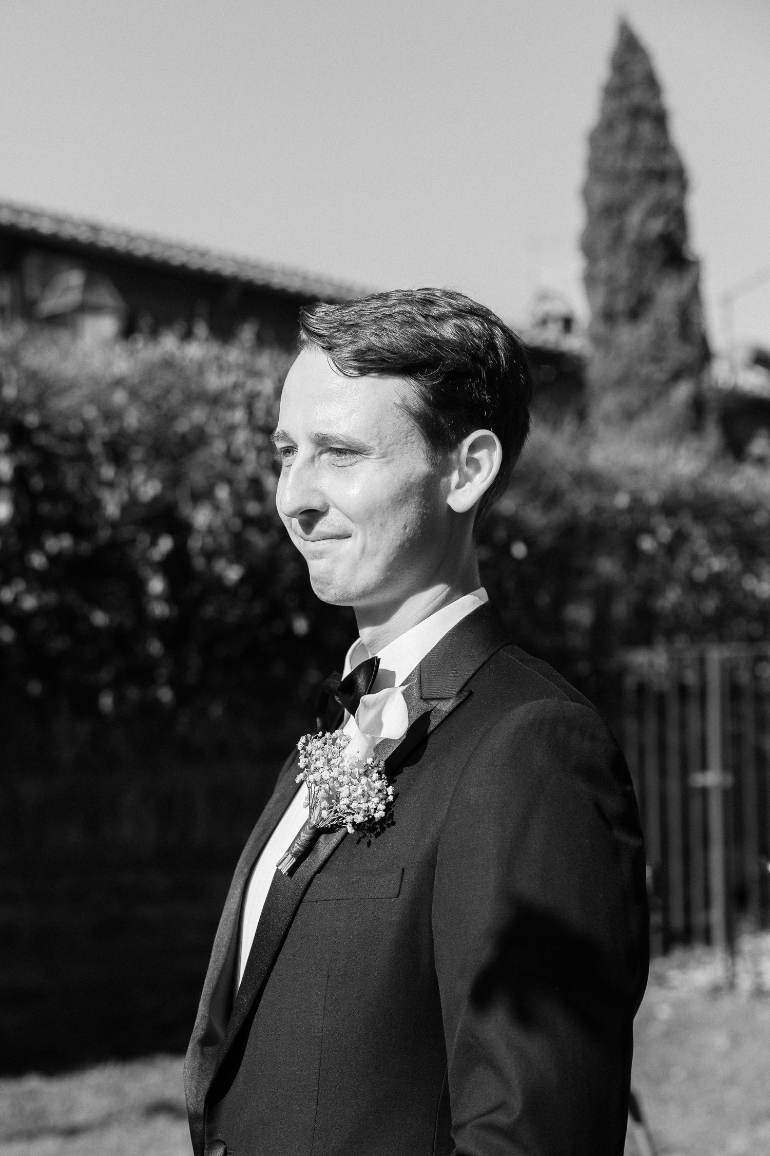Black and white portrait of a groom in a tuxedo with floral boutonniere outdoors on his wedding day.