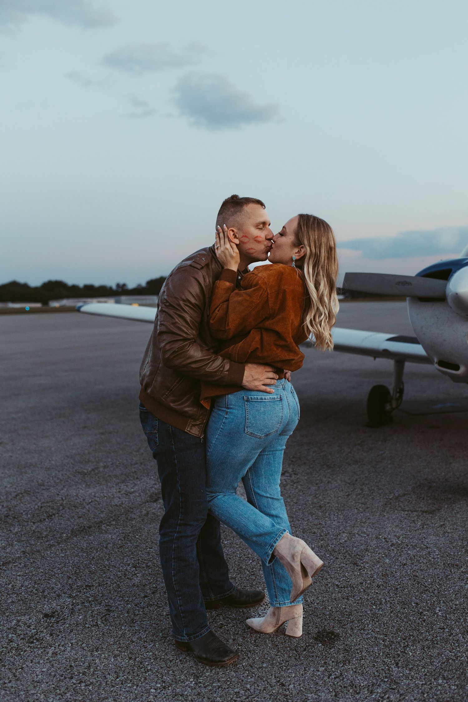 A romantic embrace captured on an airport tarmac with a small aircraft in the background.
