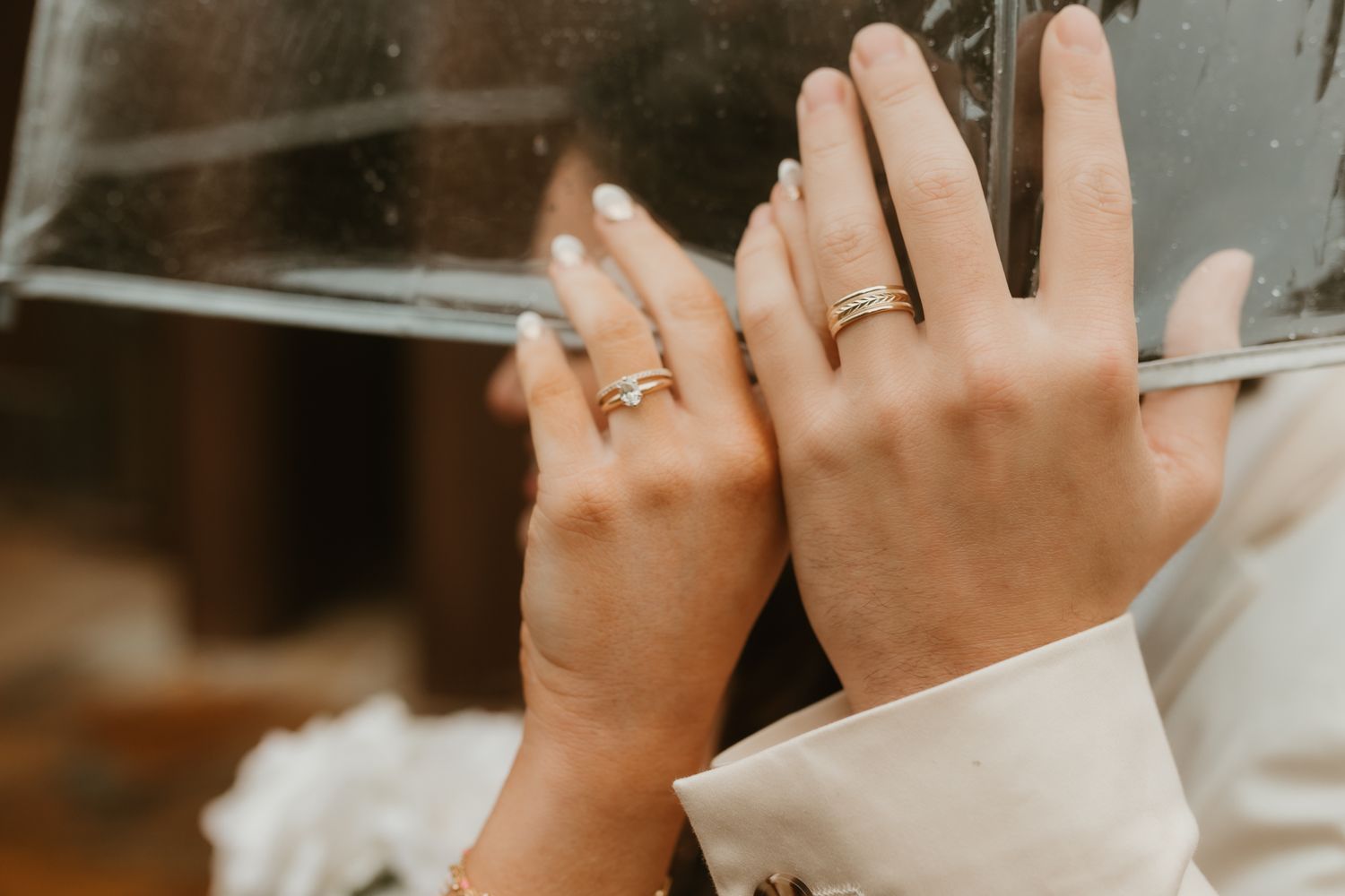 Close-up of hands with wedding rings showing through soft window light.