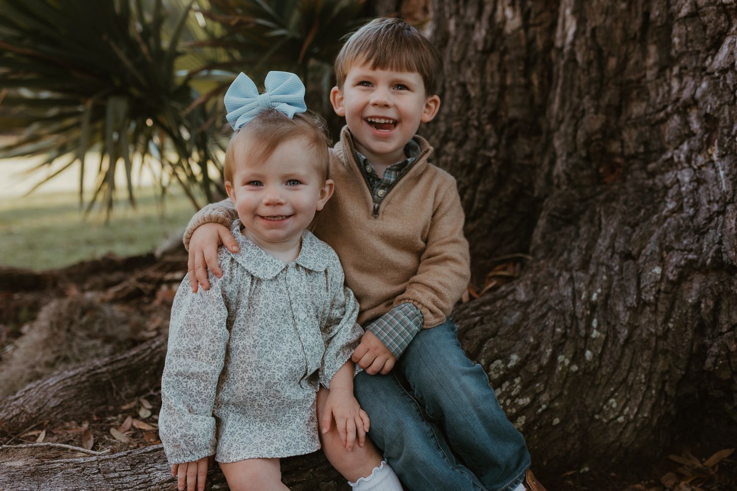 Two children sitting by a tree trunk sharing a happy moment together outdoors.