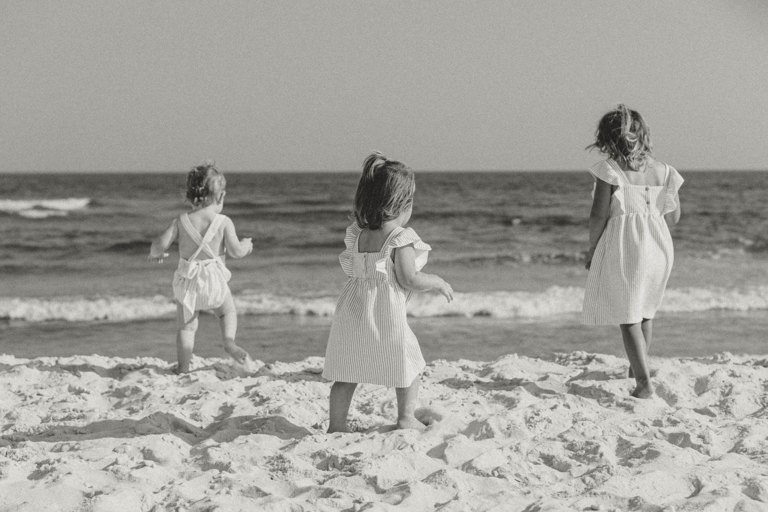 Children run and play along a sandy beach in black and white.