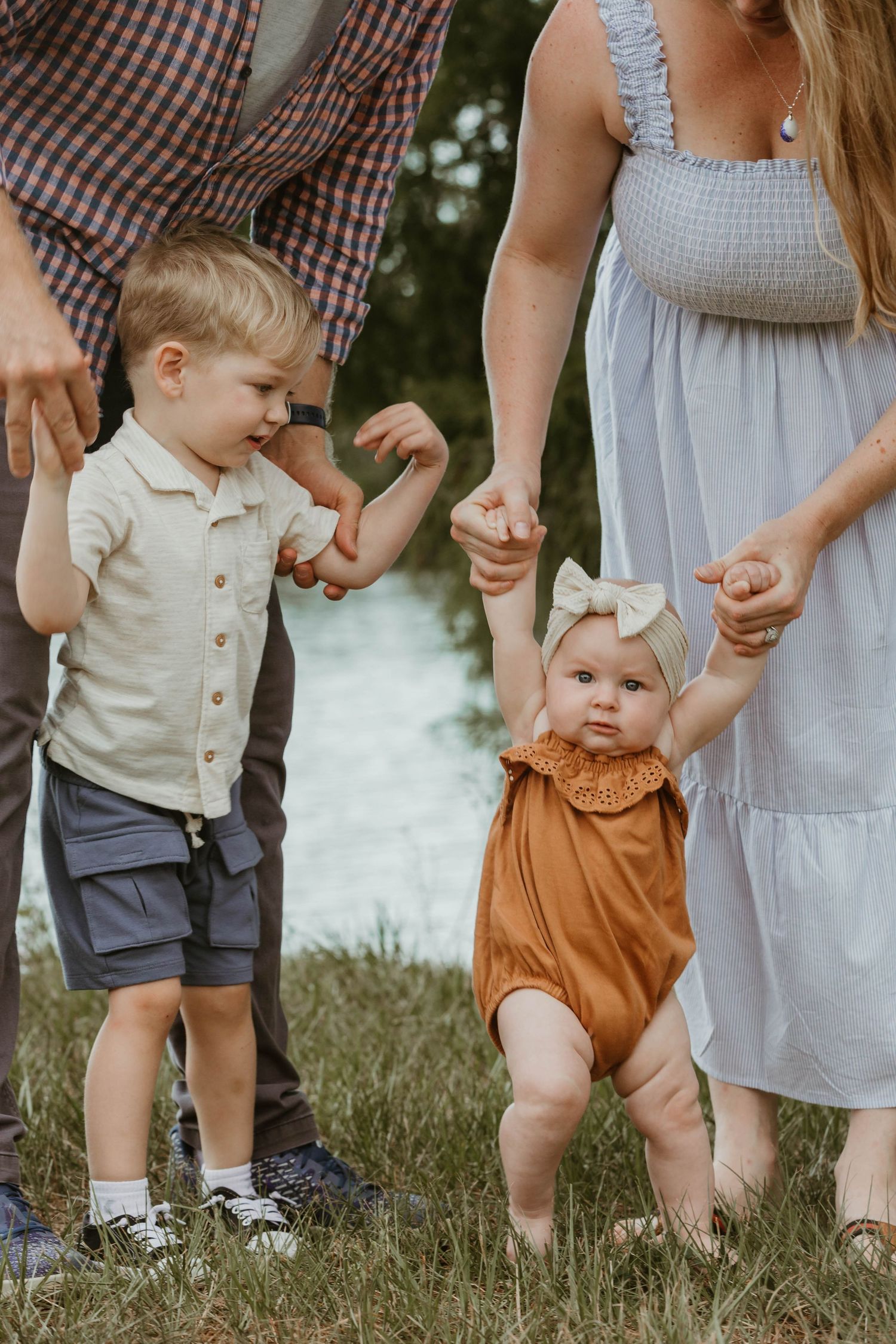 A sweet moment of family holding hands together in a grassy field by water.