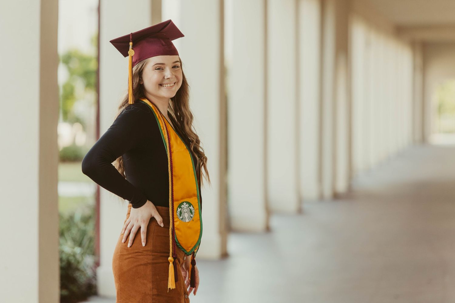 Graduate in cap and gown poses in front of white columned walkway.