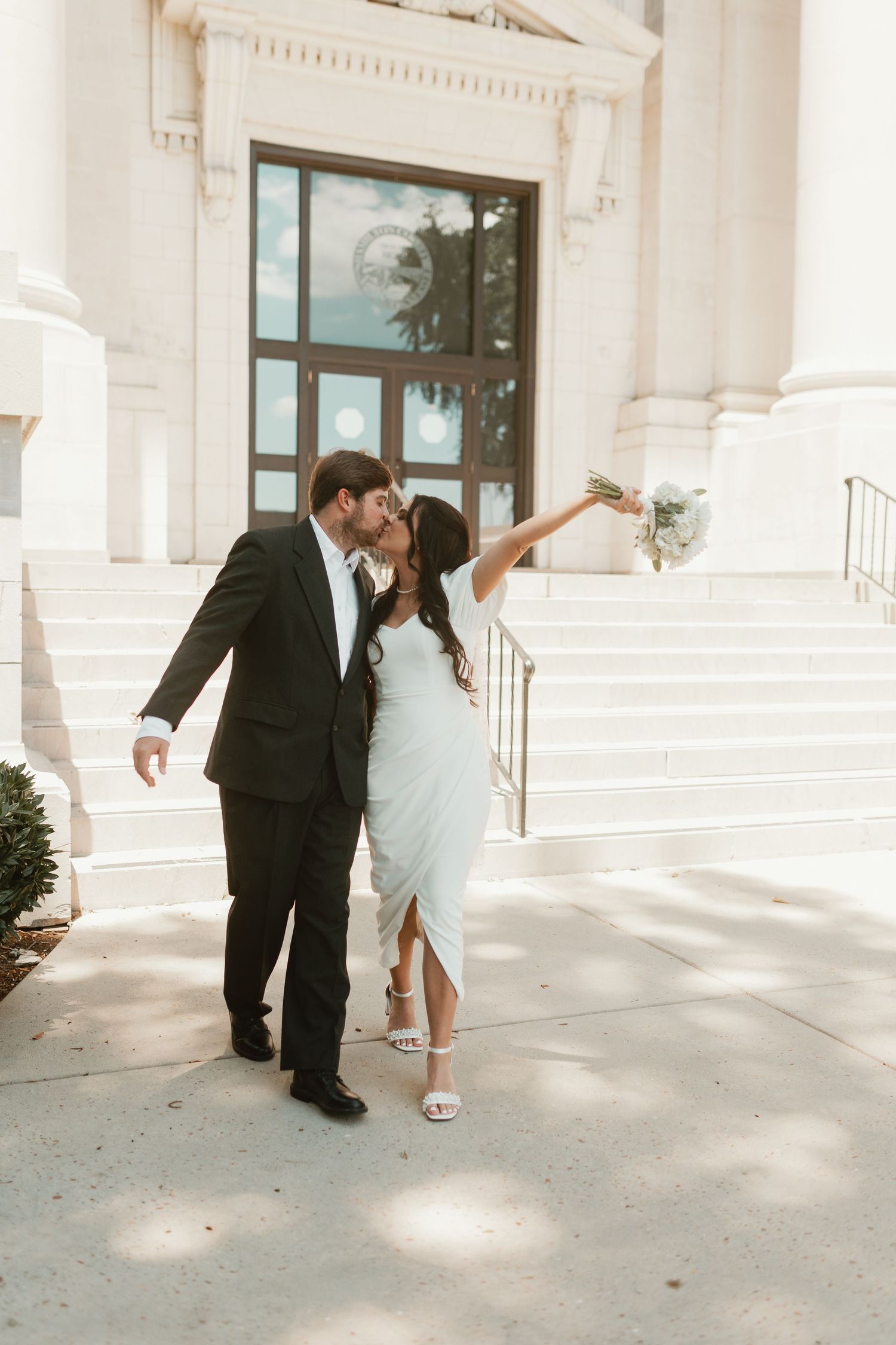 Romantic dance dip pose on marble steps of grand white building.