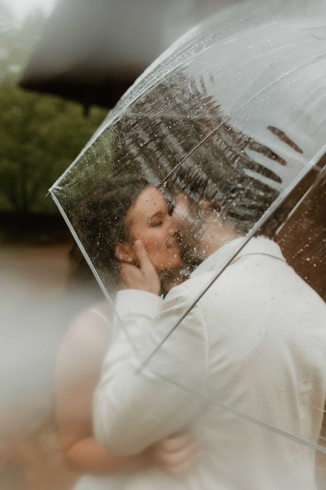 A tender embrace captured through a transparent umbrella in the rain.
