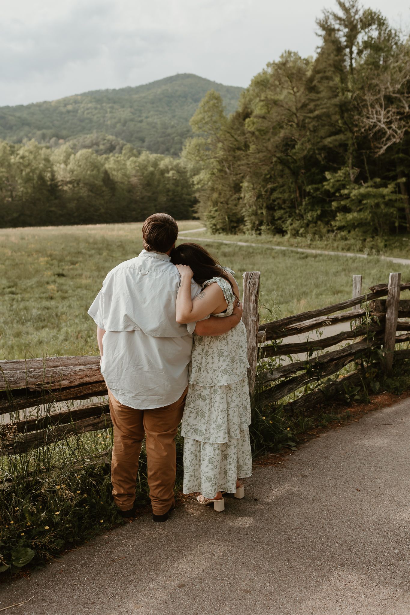 Couple enjoying scenic mountain views while leaning on a rustic wooden fence.