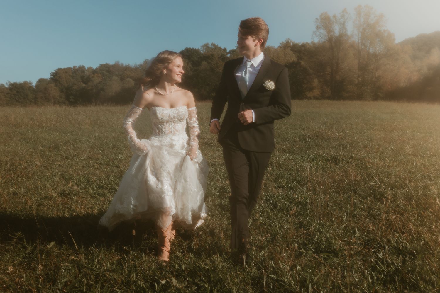 Wedding couple running playfully through a sunlit meadow.