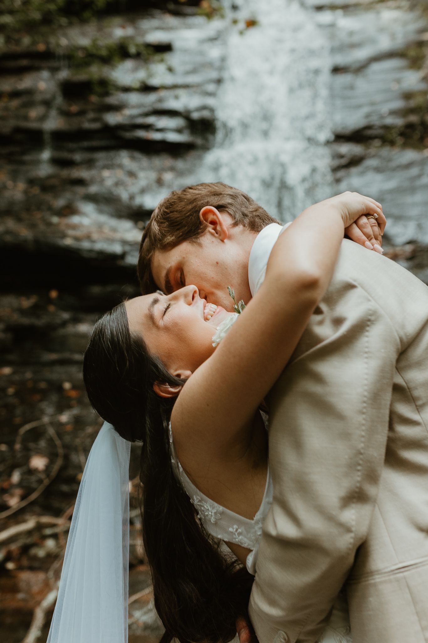 A romantic wedding kiss in front of a cascading waterfall.