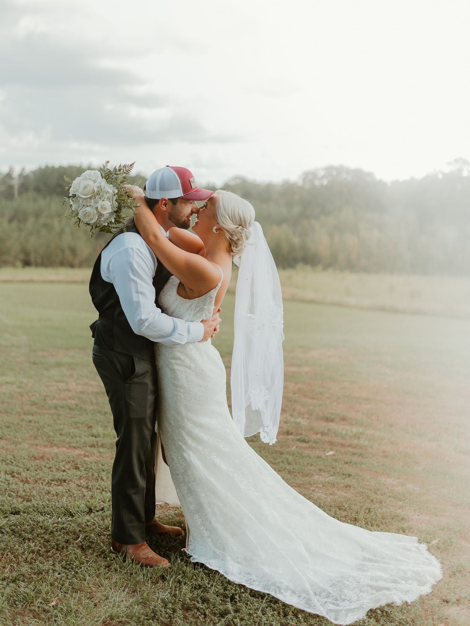 Romantic wedding couple embracing in an outdoor field during golden hour.