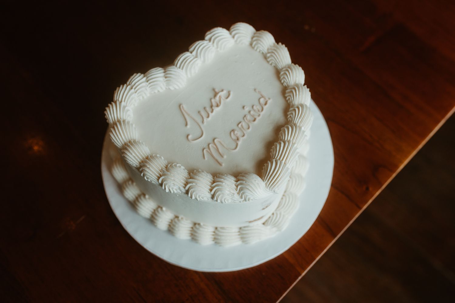 A white heart-shaped wedding cake with delicate piped details on a wooden table.