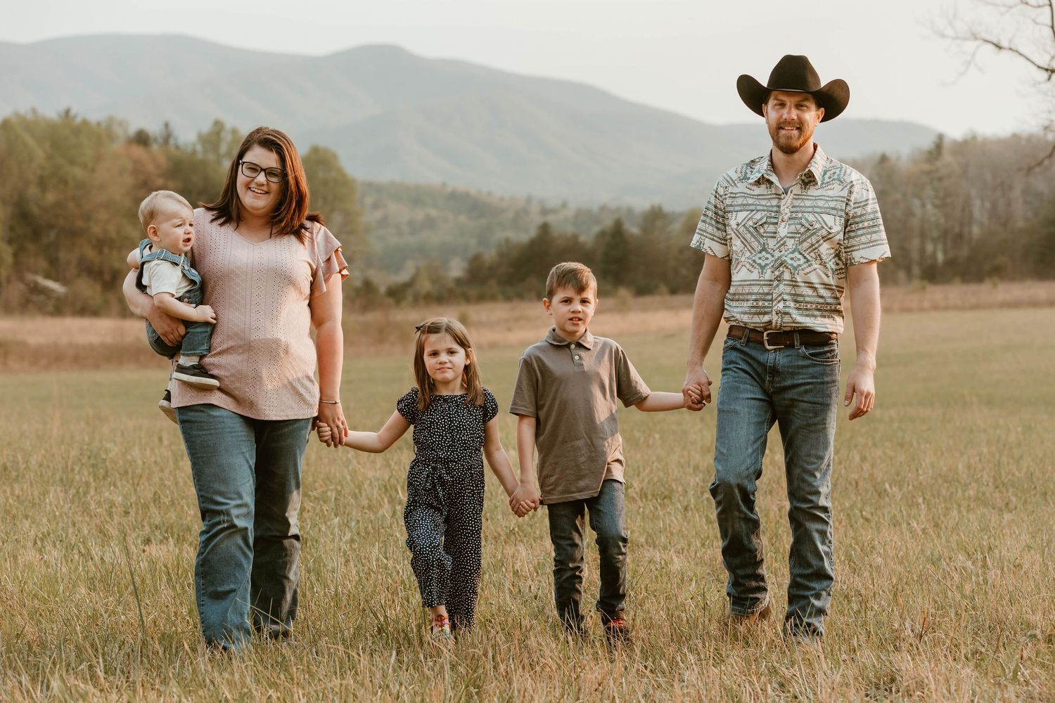 Family of five walking together through a scenic mountain field at sunset.