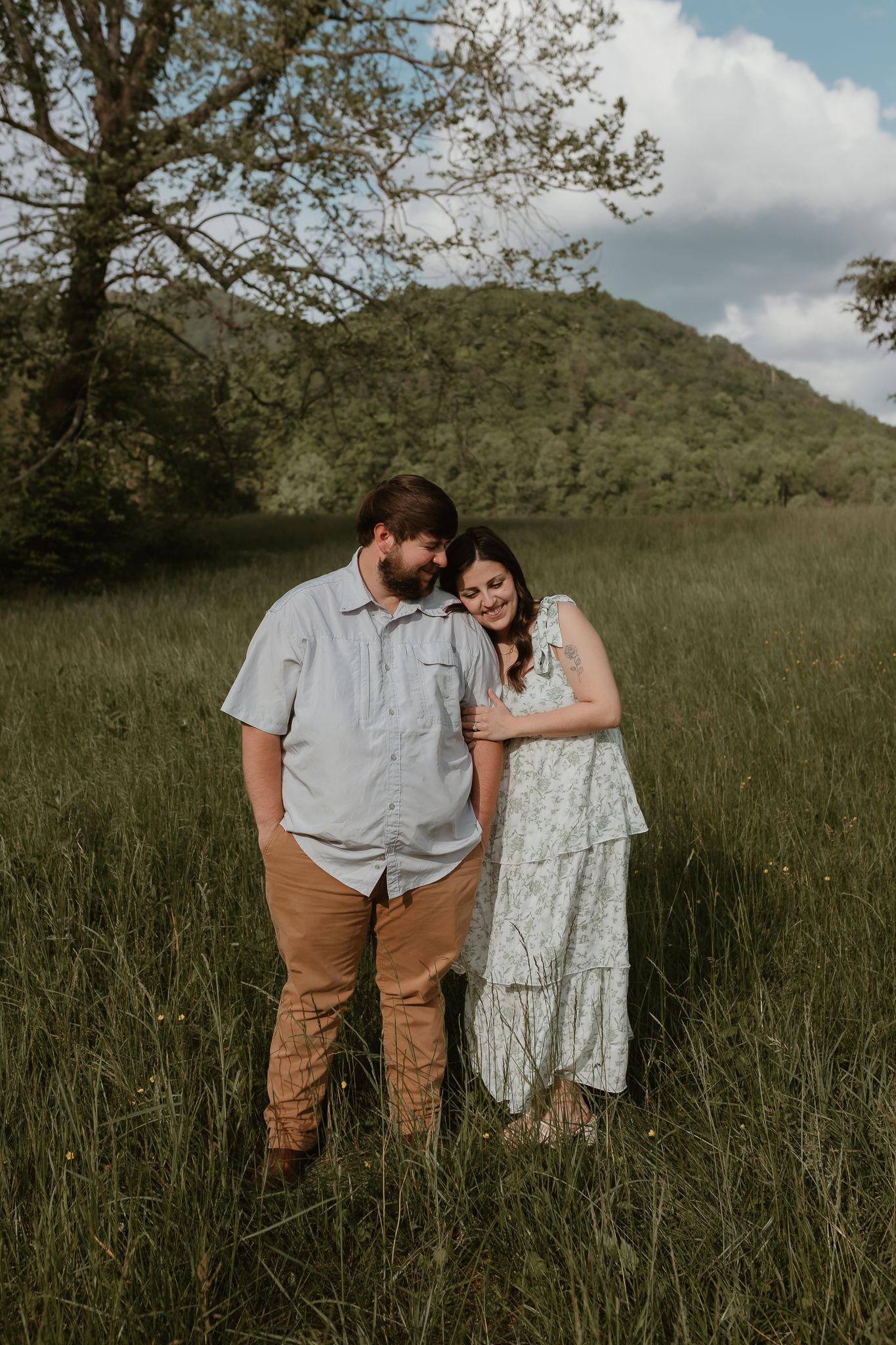 Couple sharing an intimate moment in a meadow with tall grass and cloudy skies.