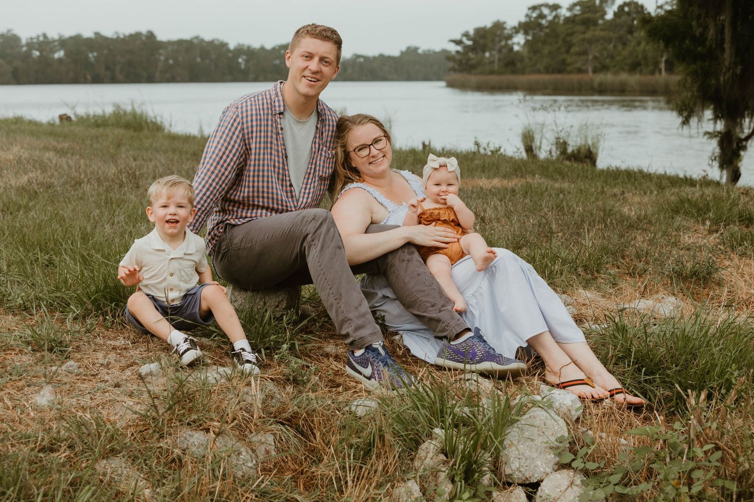 A family sits together on a grassy hill during a warm sunset photo session.