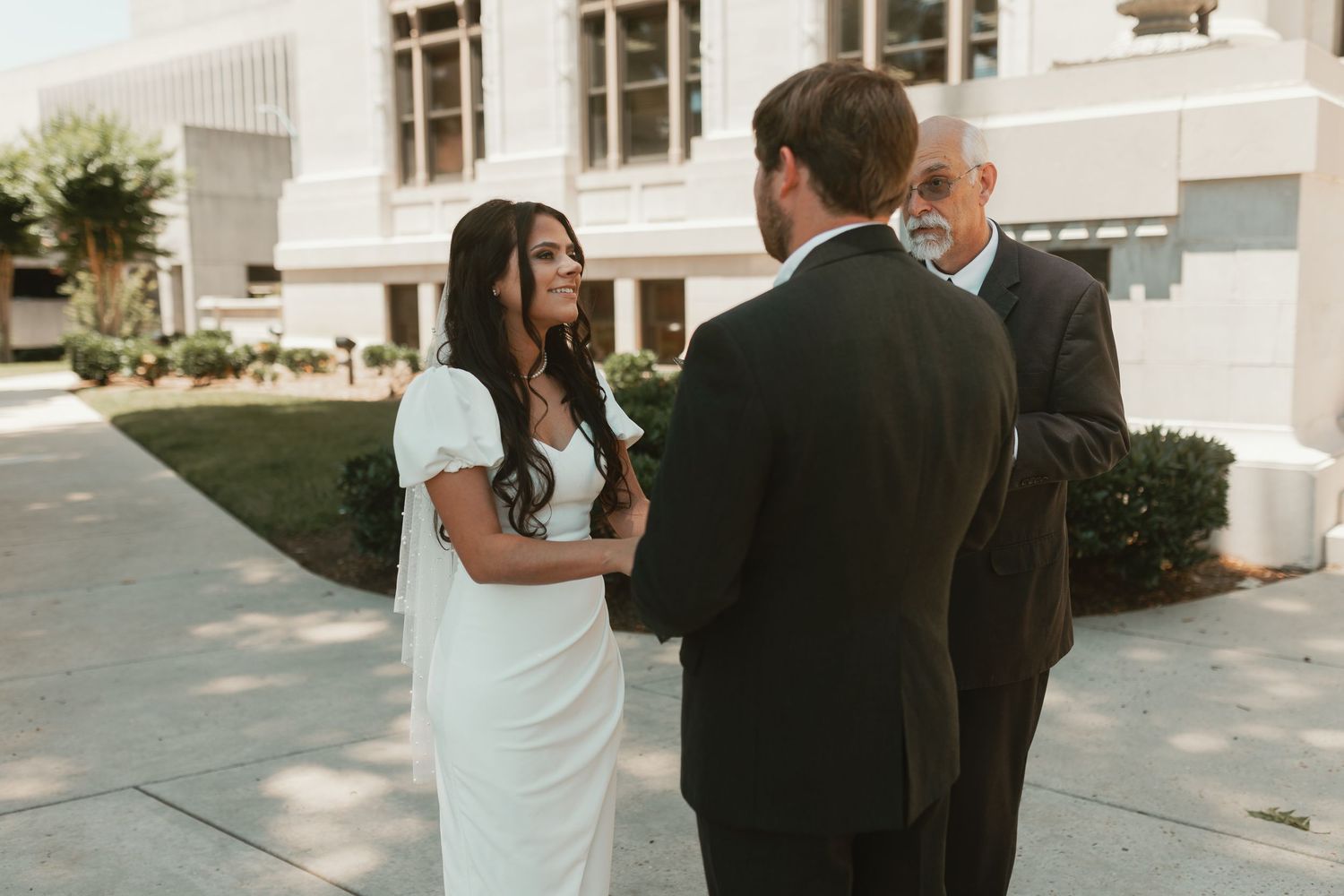 Wedding couple interacts outside a historic courthouse building with white columns.