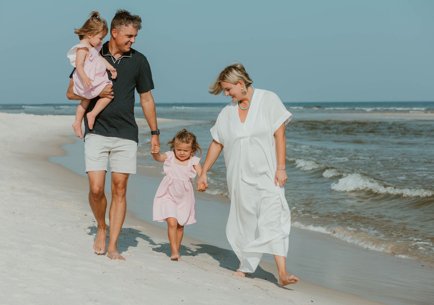 Family members walking along a beach shoreline with waves in the background.