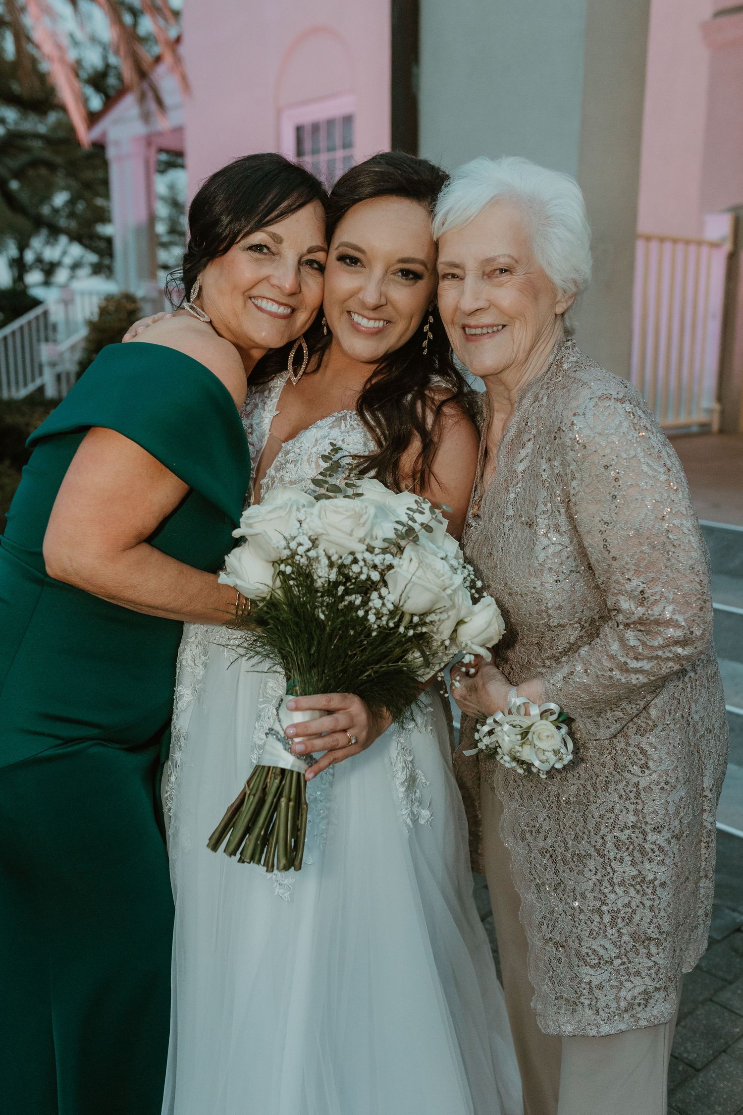 Three generations celebrate at a wedding with bouquet and formal dresses.