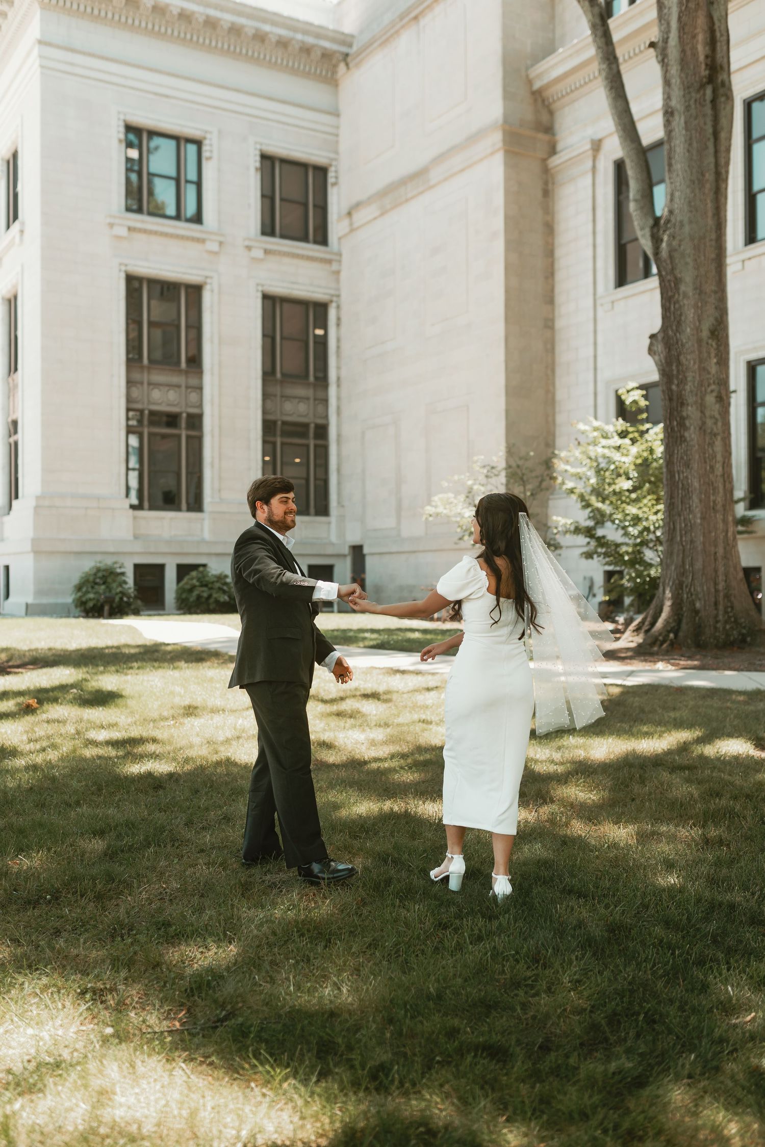 Couple shares a playful first look moment on the lawn of a grand white columned building.